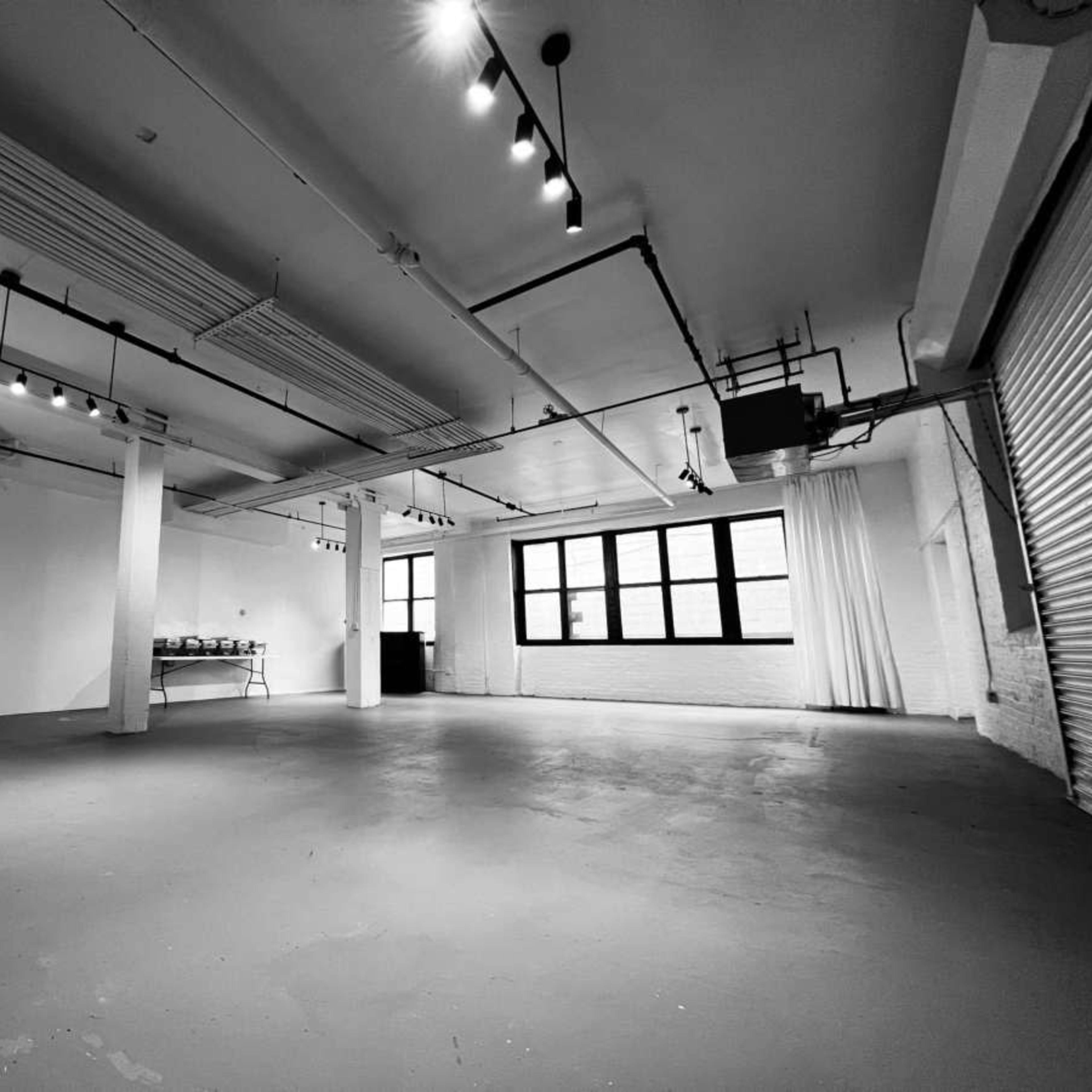 A spacious, empty room with white walls, concrete flooring, and overhead lighting.