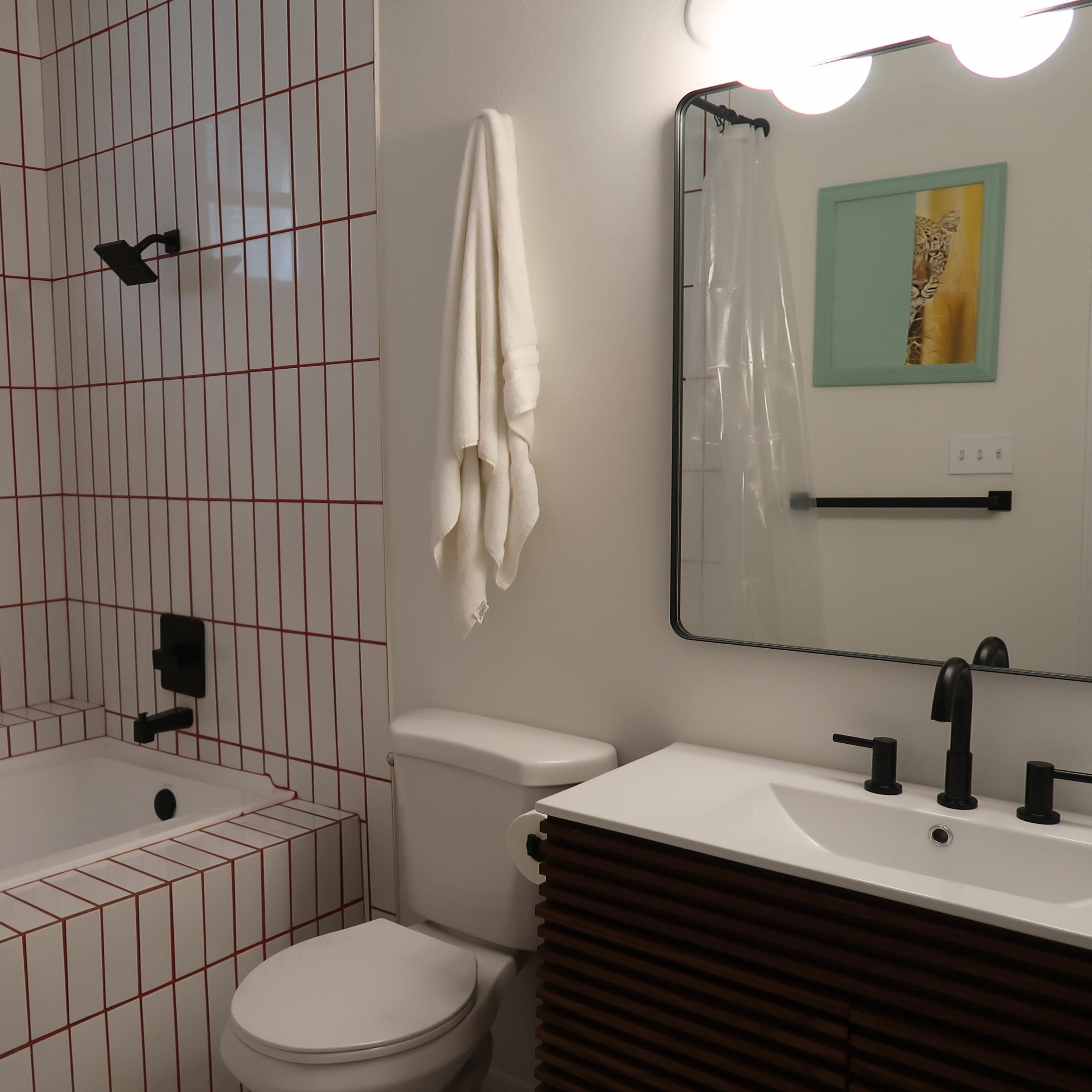 The bathroom features a tub-shower combo with red-grid tile, a wall-mounted mirror, a modern sink with dark fixtures, and a white towel hanging on a hook.