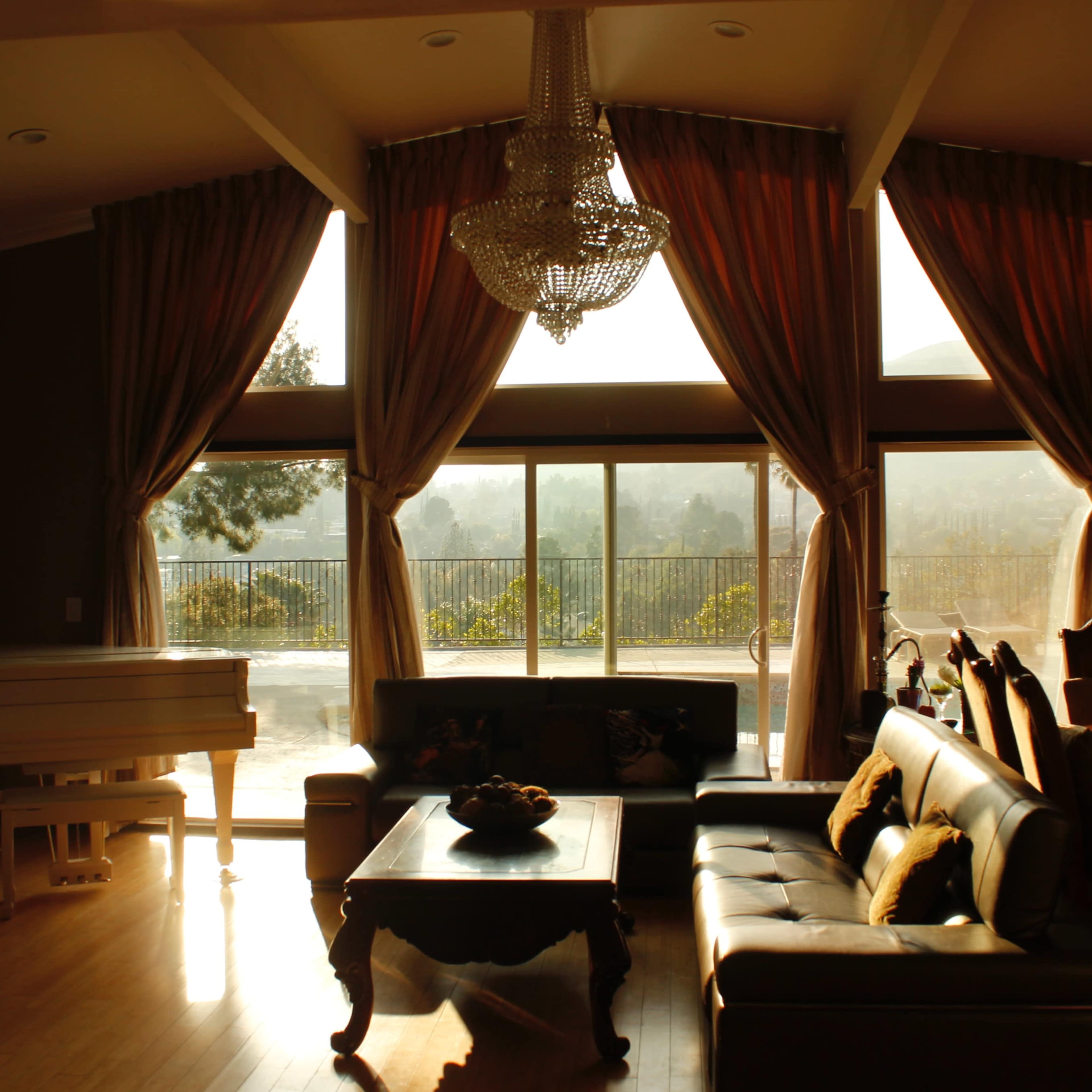 A spacious living room features a grand piano, a coffee table, and large windows that overlook a scenic view, illuminated by soft natural light.