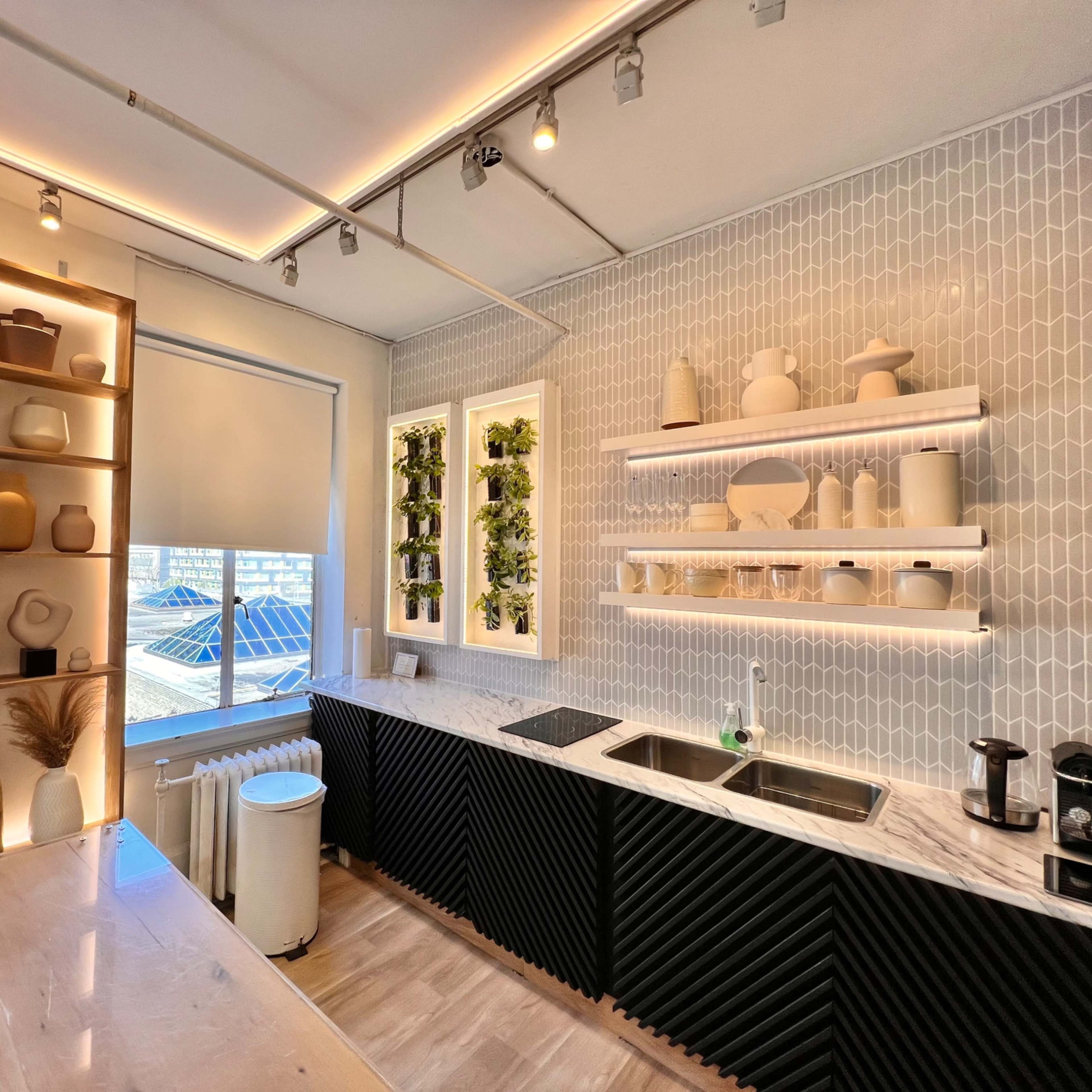 A modern kitchen with a marble countertop, a black textured cabinet, and decorative shelves displaying various ceramic vases and plants.