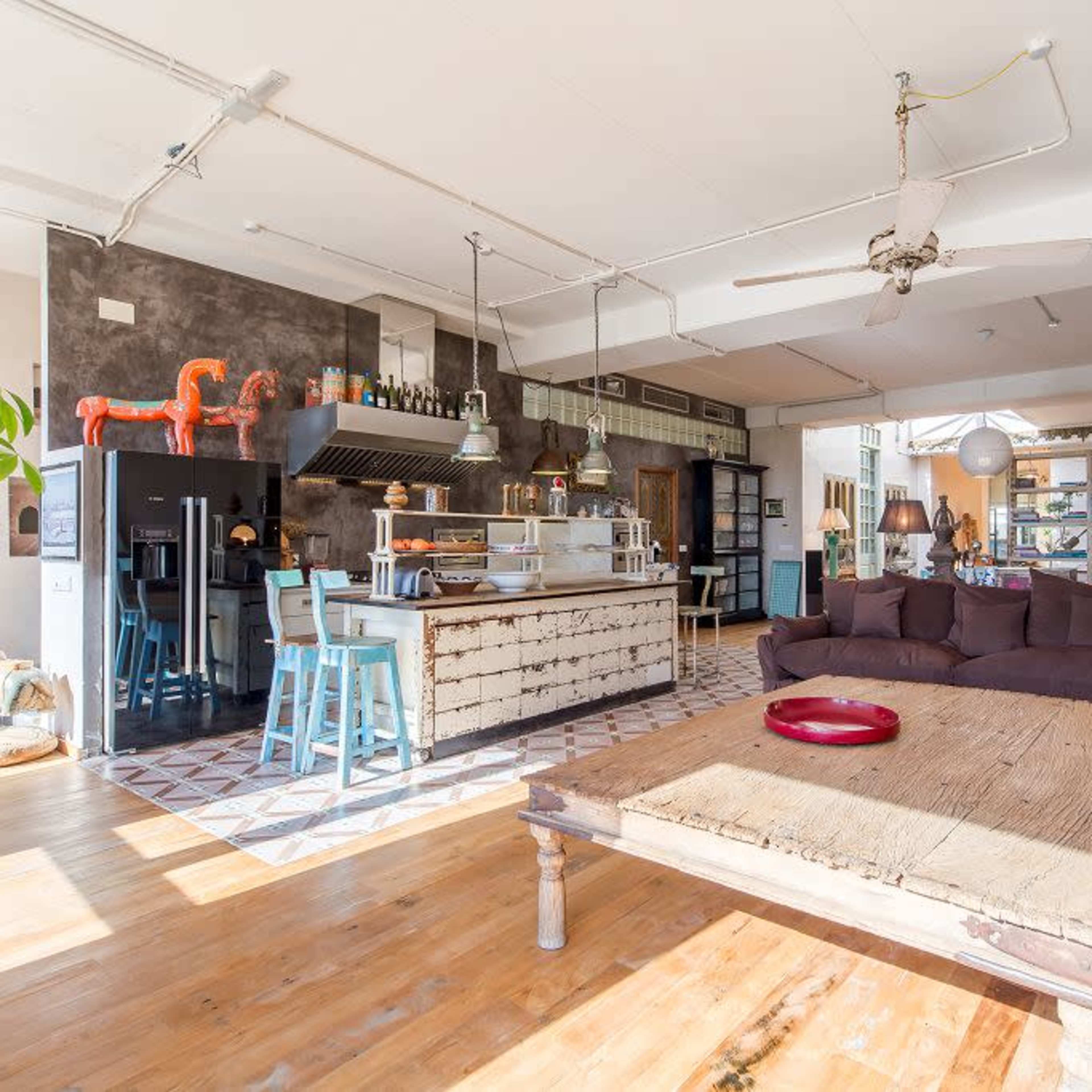 A spacious, modern open-concept living area with a large wooden table, a sectional sofa, and a well-equipped kitchen in the background.