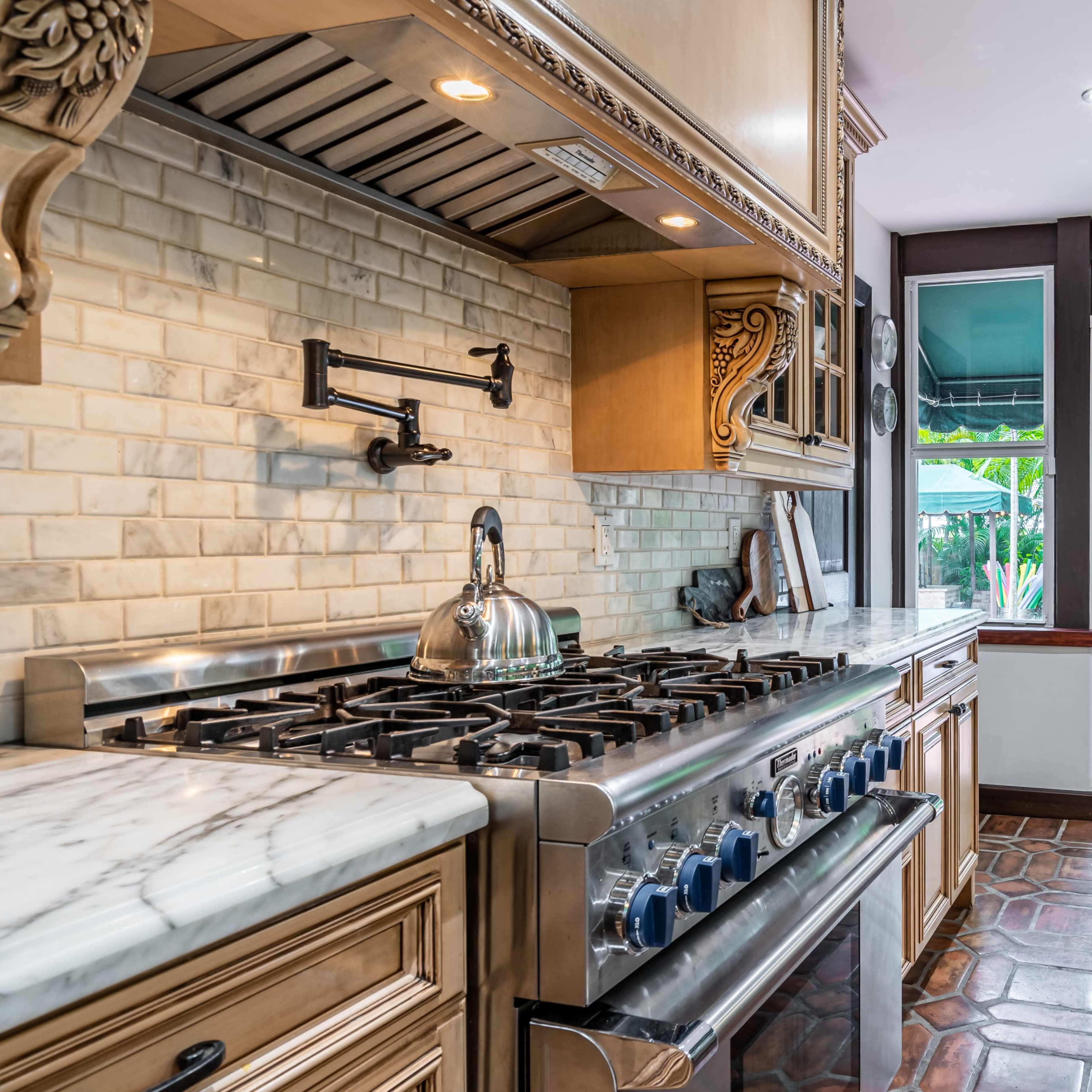 A kitchen with a marble countertop, a gas stove with multiple burners, and double doors leading to an outdoor seating area.