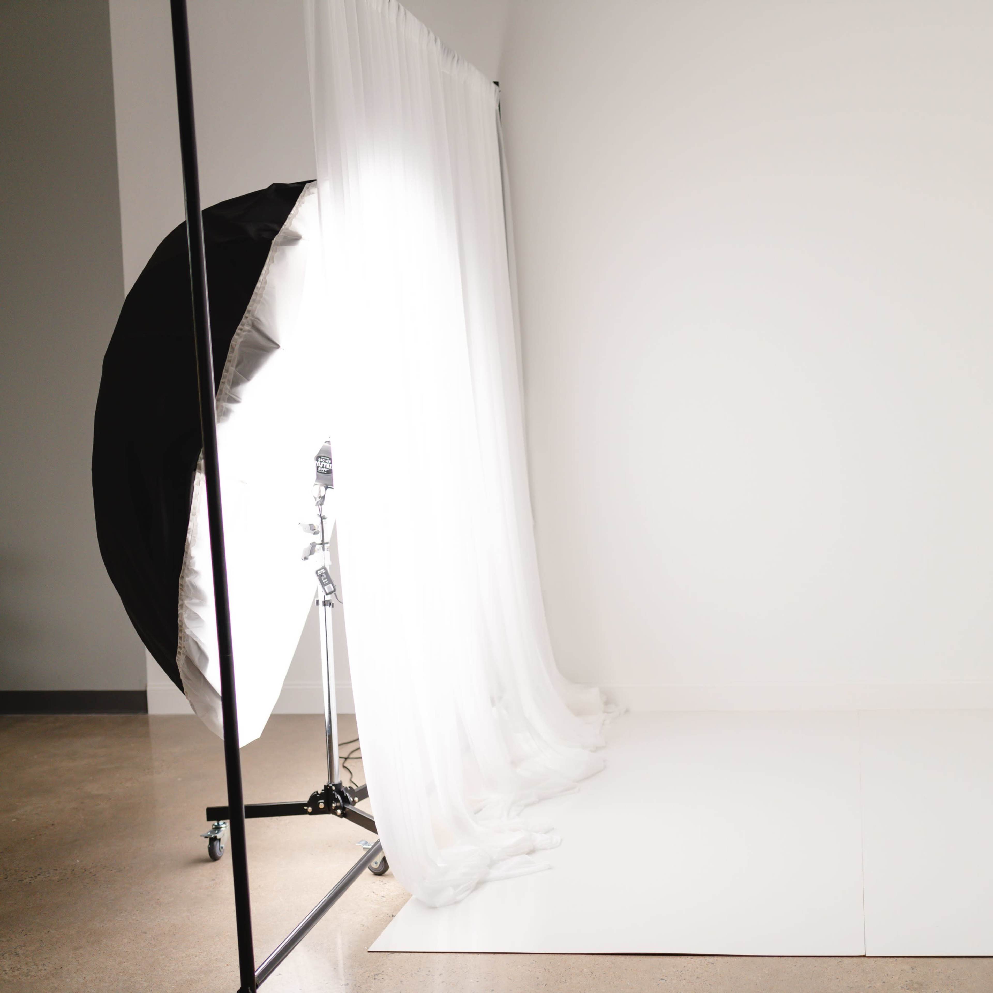 A minimalist photography studio with a plain white backdrop and soft curtains.