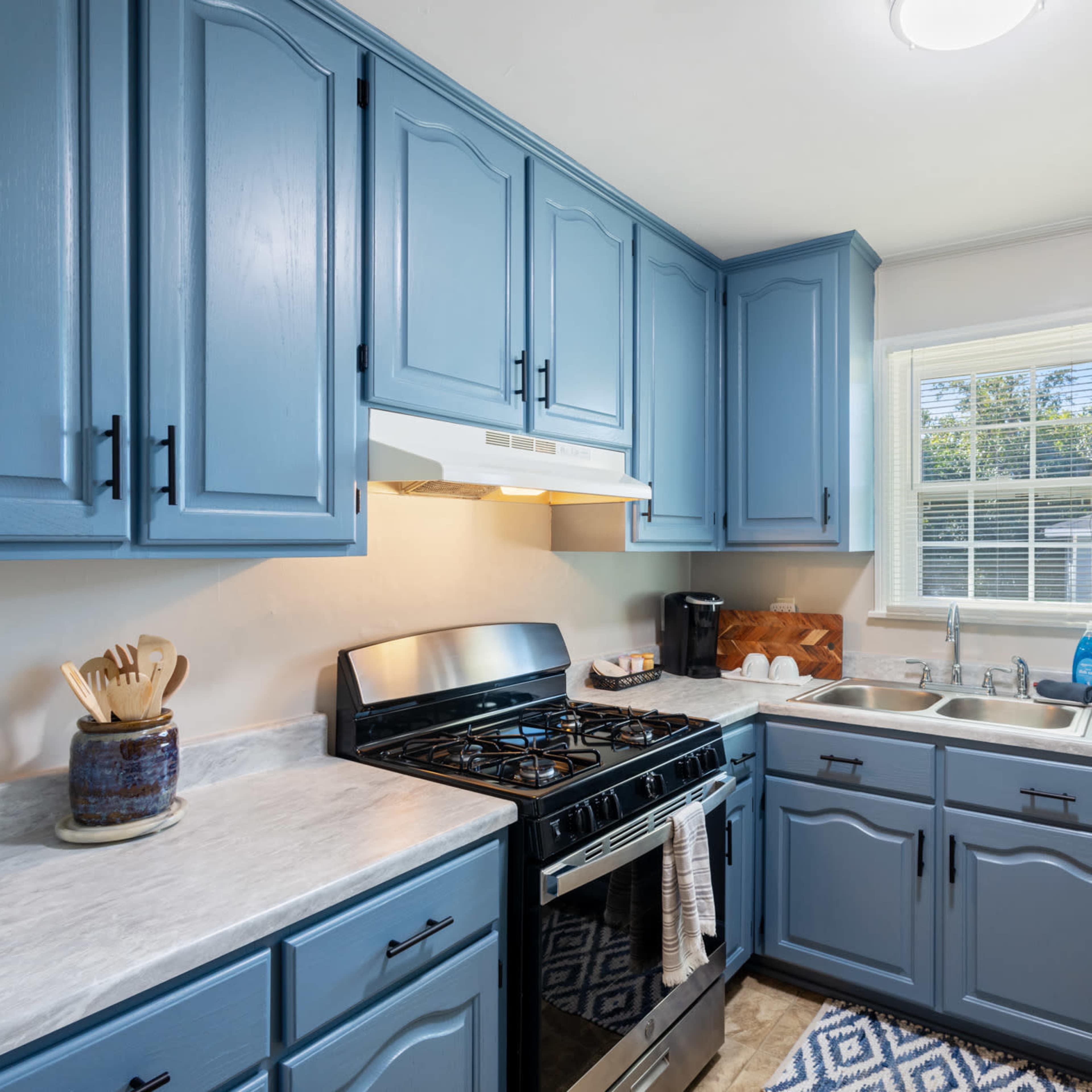 A modern kitchen with blue cabinetry, a gas stove, and a sink under a window.