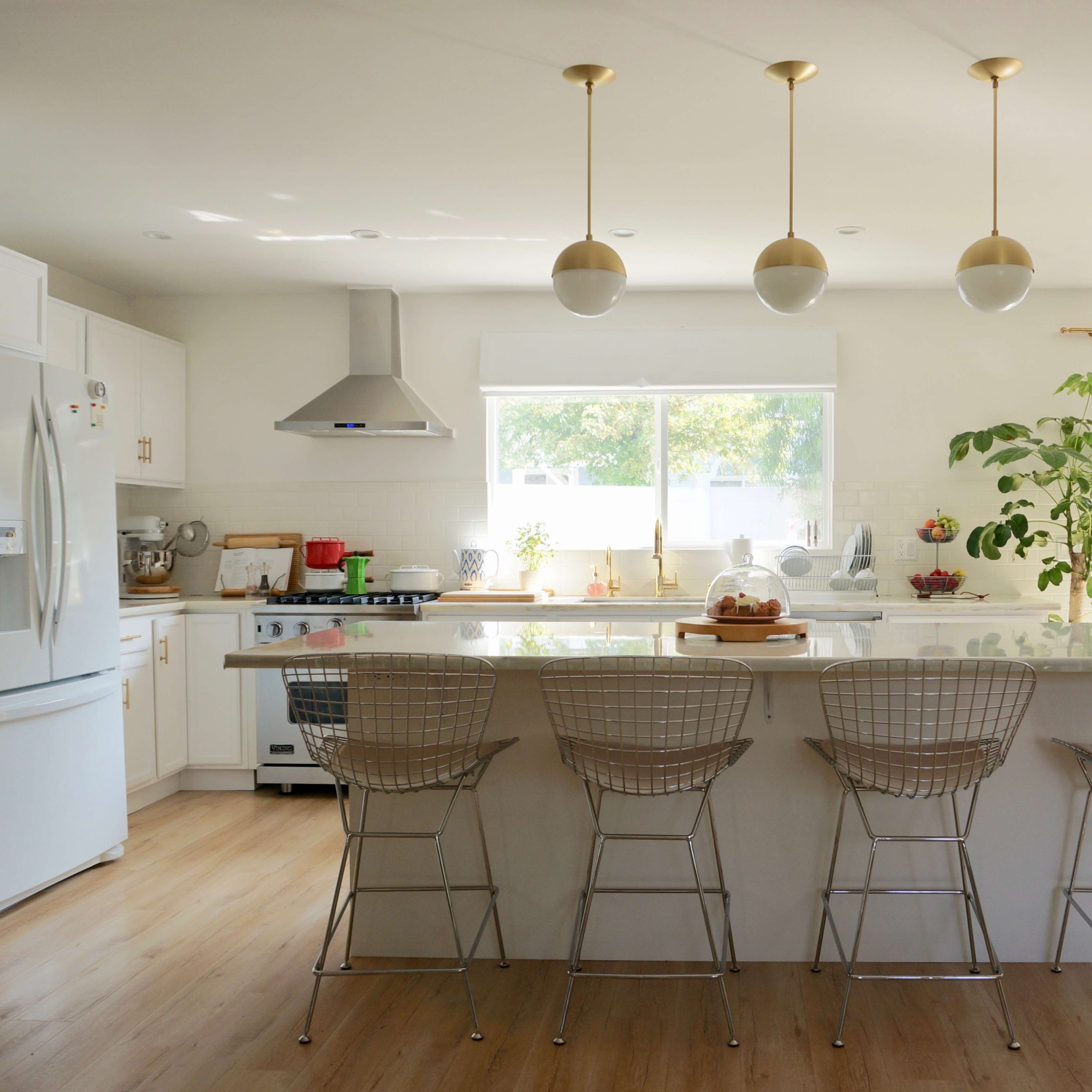 A modern kitchen with a large island, metallic bar stools, and ample natural light from a window and sliding doors.