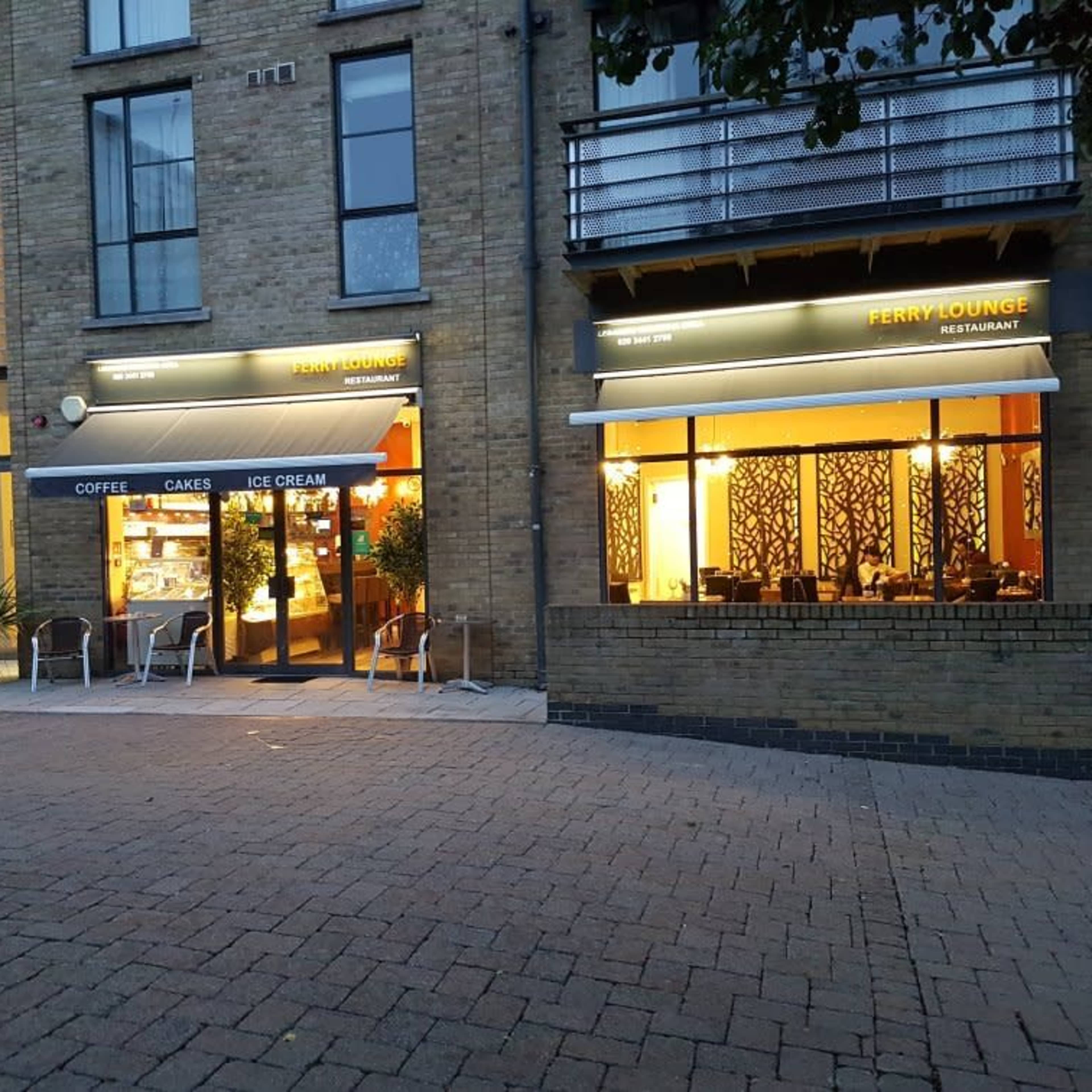 A building with two restaurant entrances, Ferry Lounge and another café, set in a brick exterior with outdoor seating.