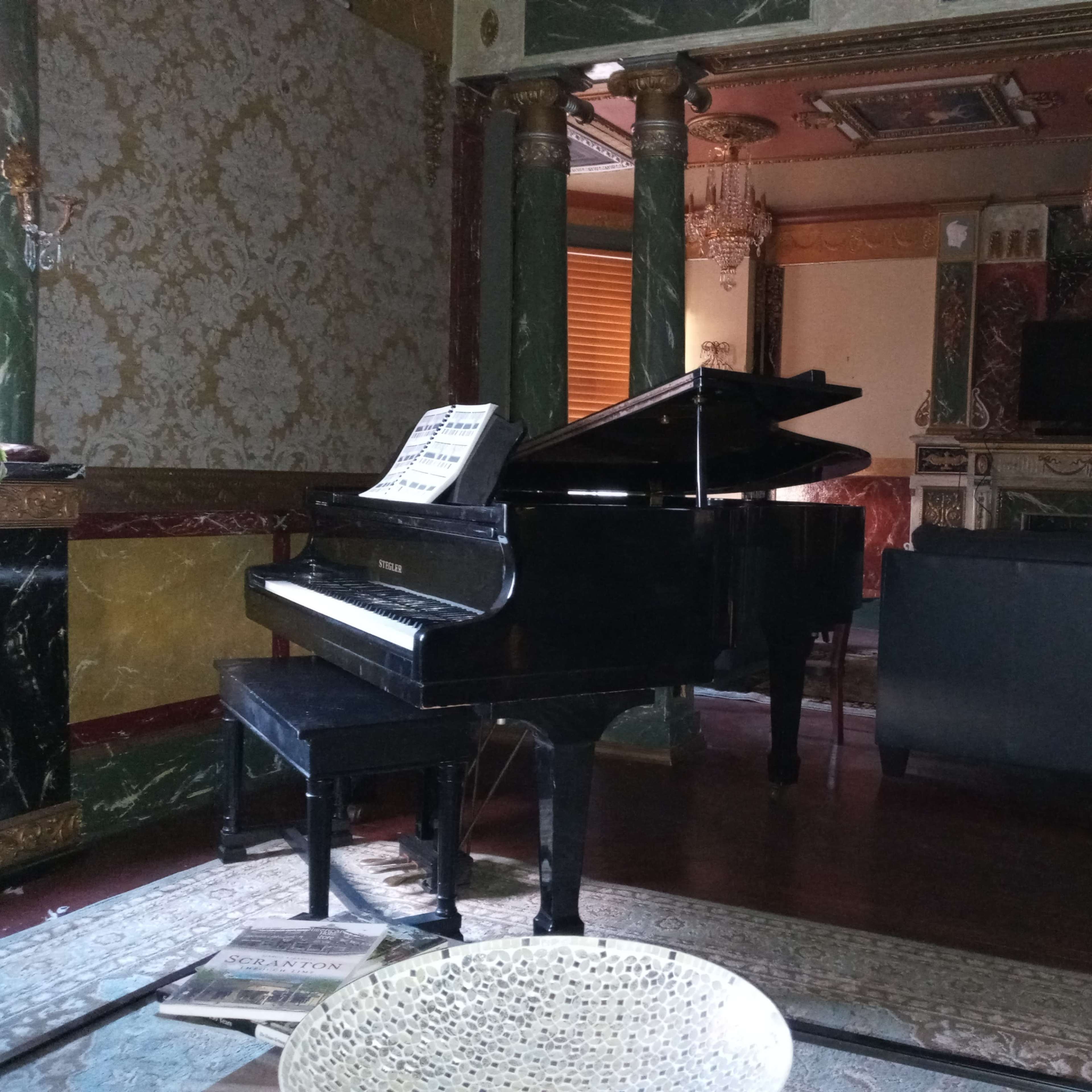 A black grand piano sits in a lavishly decorated room with ornate walls and a large fireplace.
