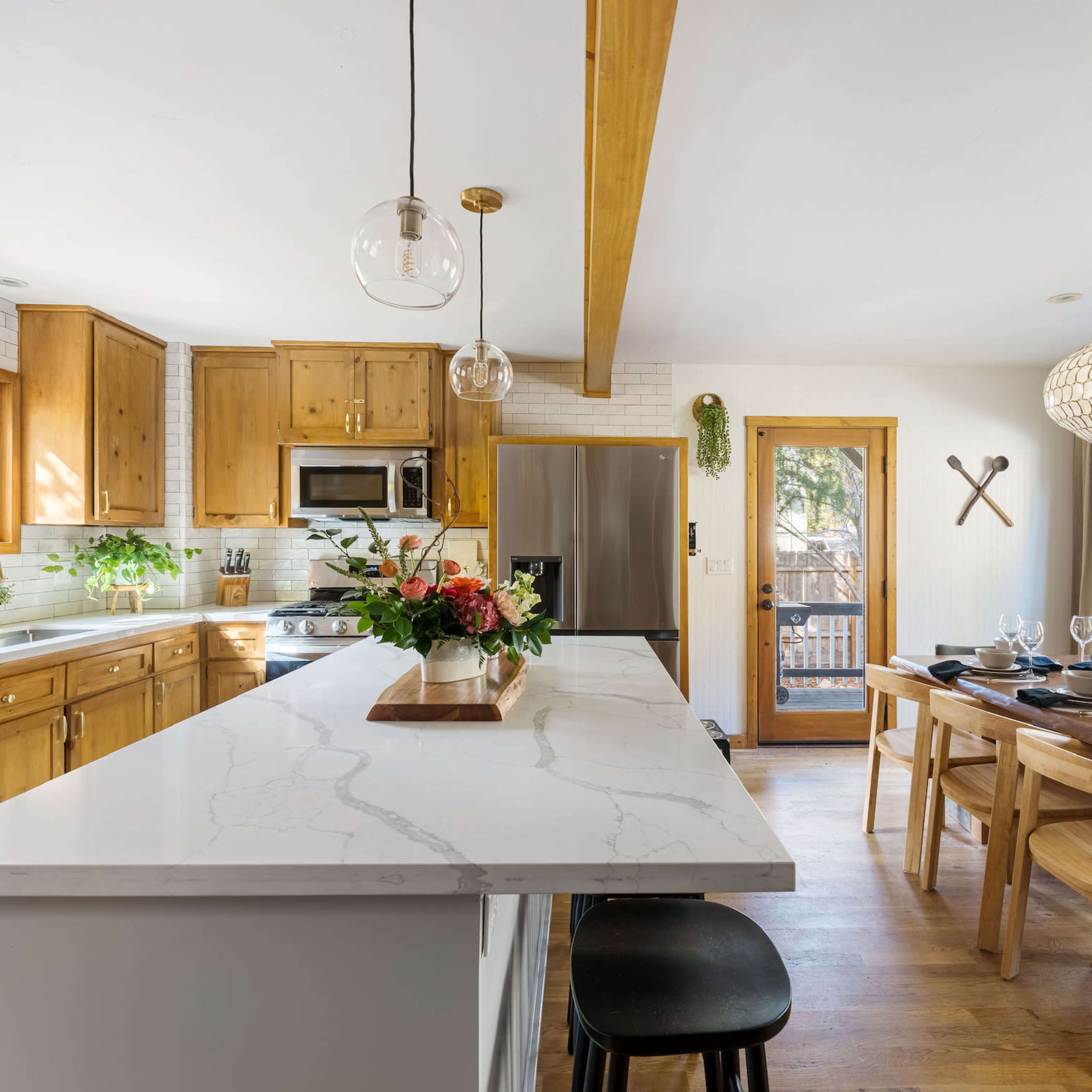 A modern kitchen features wooden cabinetry, a marble countertop island, and a dining area with a wooden table set for a meal.