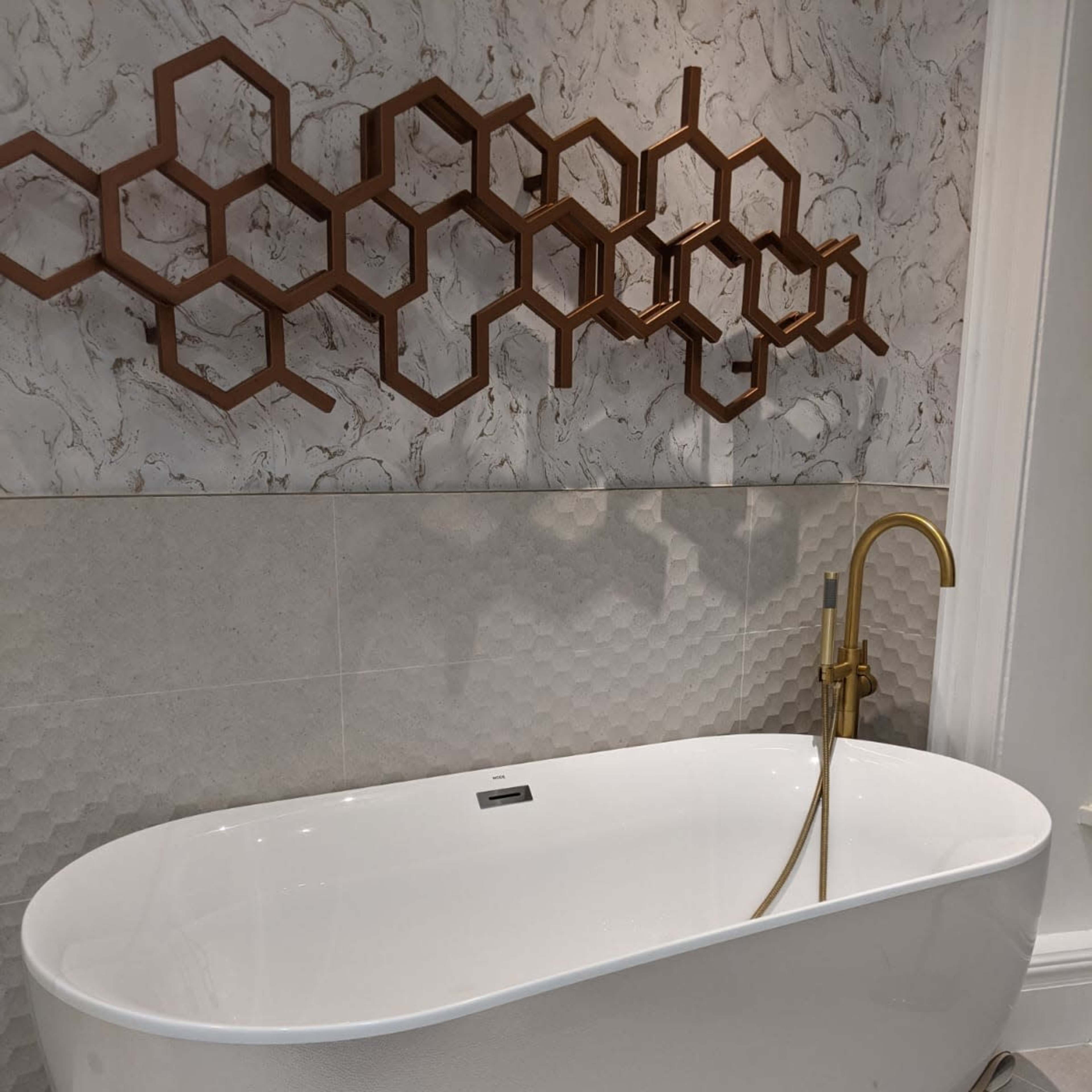A modern bathroom featuring a freestanding white bathtub complemented by a gold faucet and a decorative hexagonal wall piece.