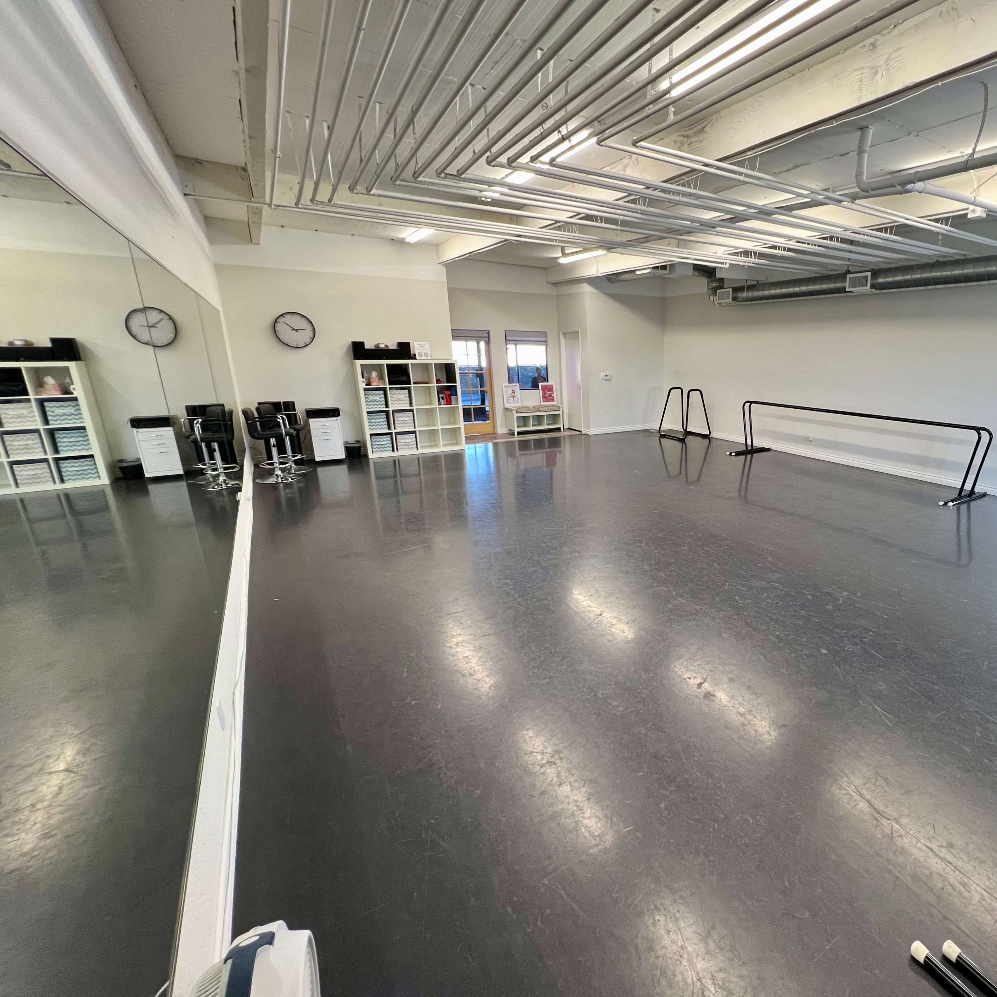 A spacious dance studio with a polished floor, mirrors on one wall, and two ballet barres along the opposite side.