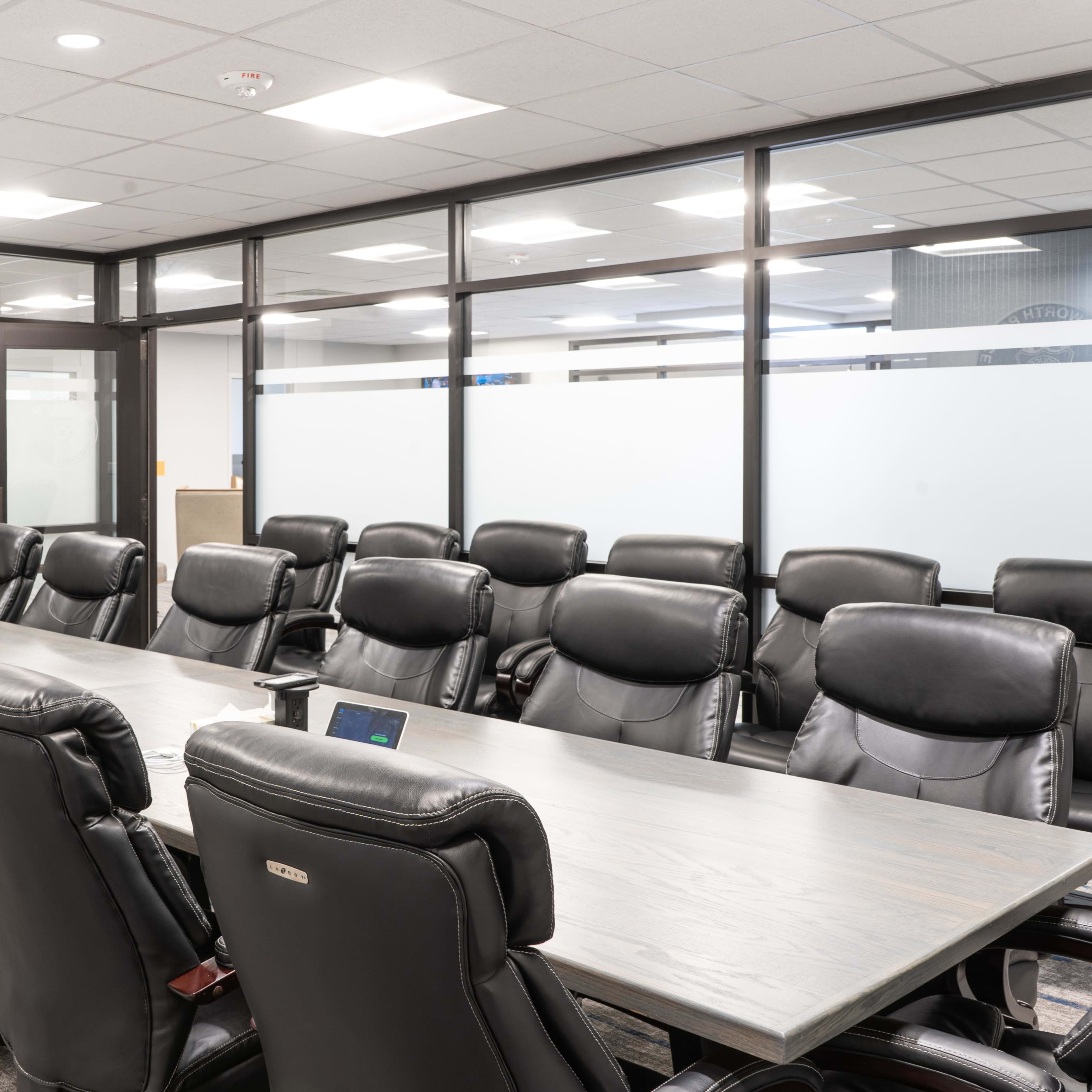 A conference room featuring a long wooden table surrounded by black leather chairs and a flat-screen television mounted on the wall.