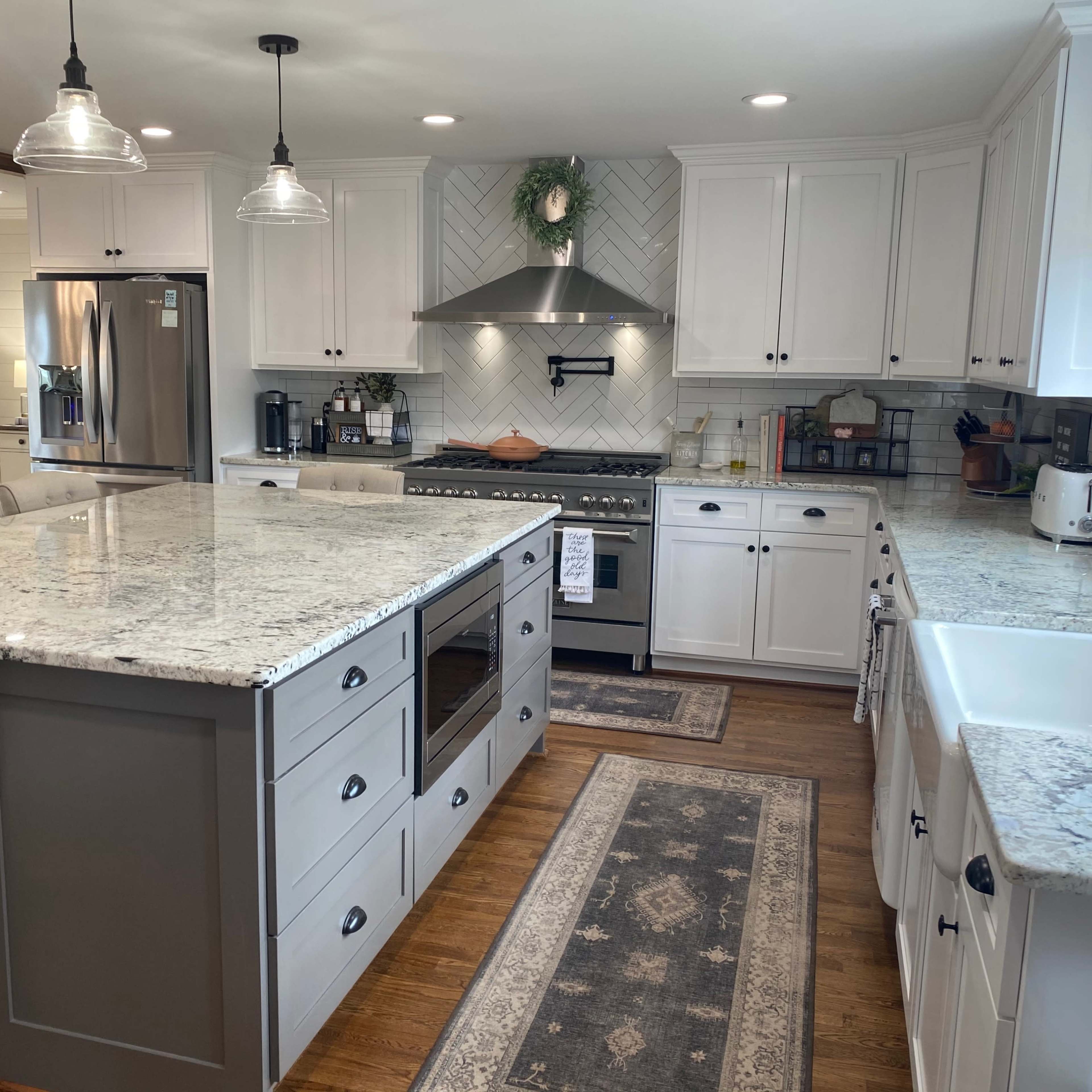 The kitchen features a large island with a gray base, white cabinetry, granite countertops, a stainless steel stove, and a farmhouse sink.