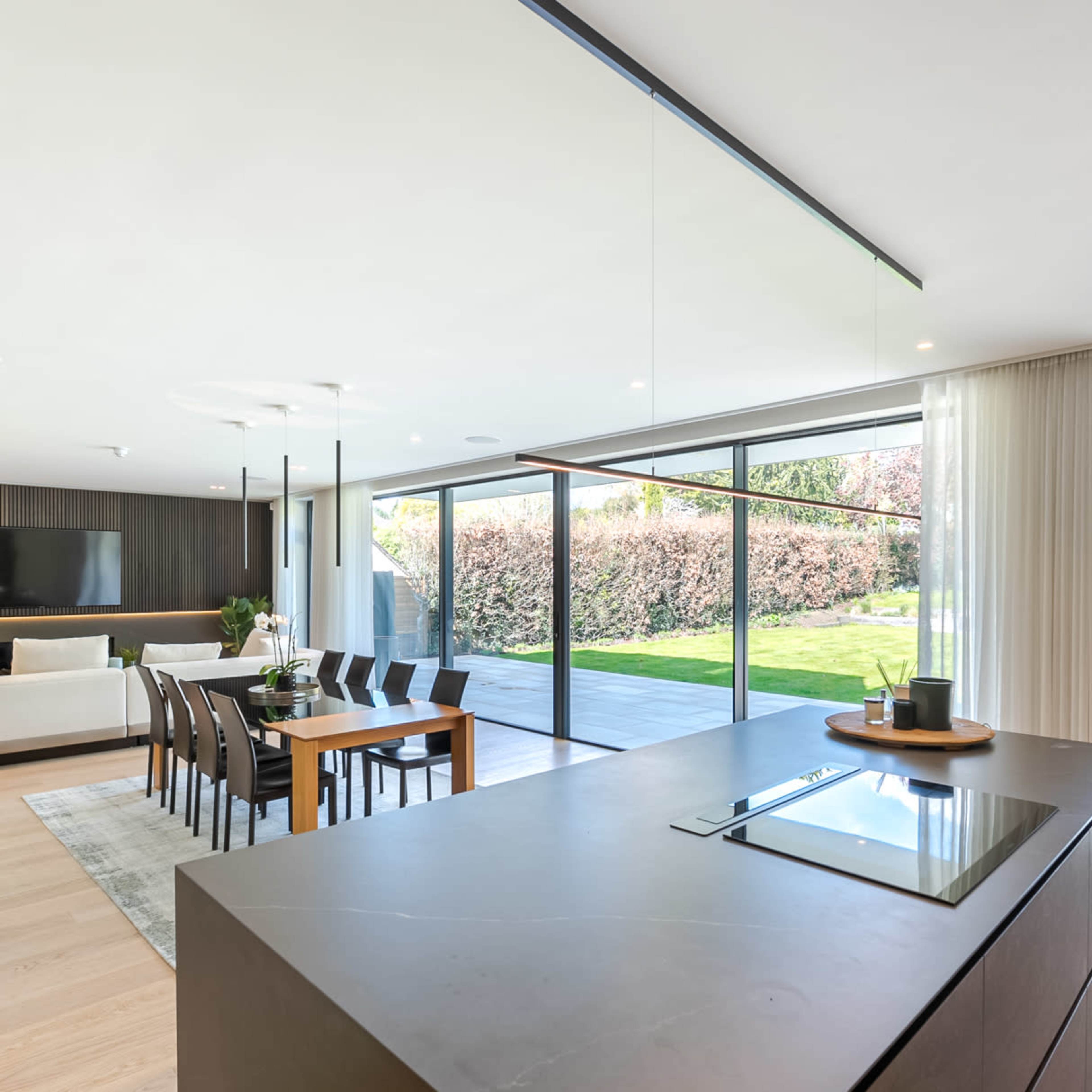 A modern, open-plan kitchen and dining area that connects to a spacious outdoor patio through large glass sliding doors.