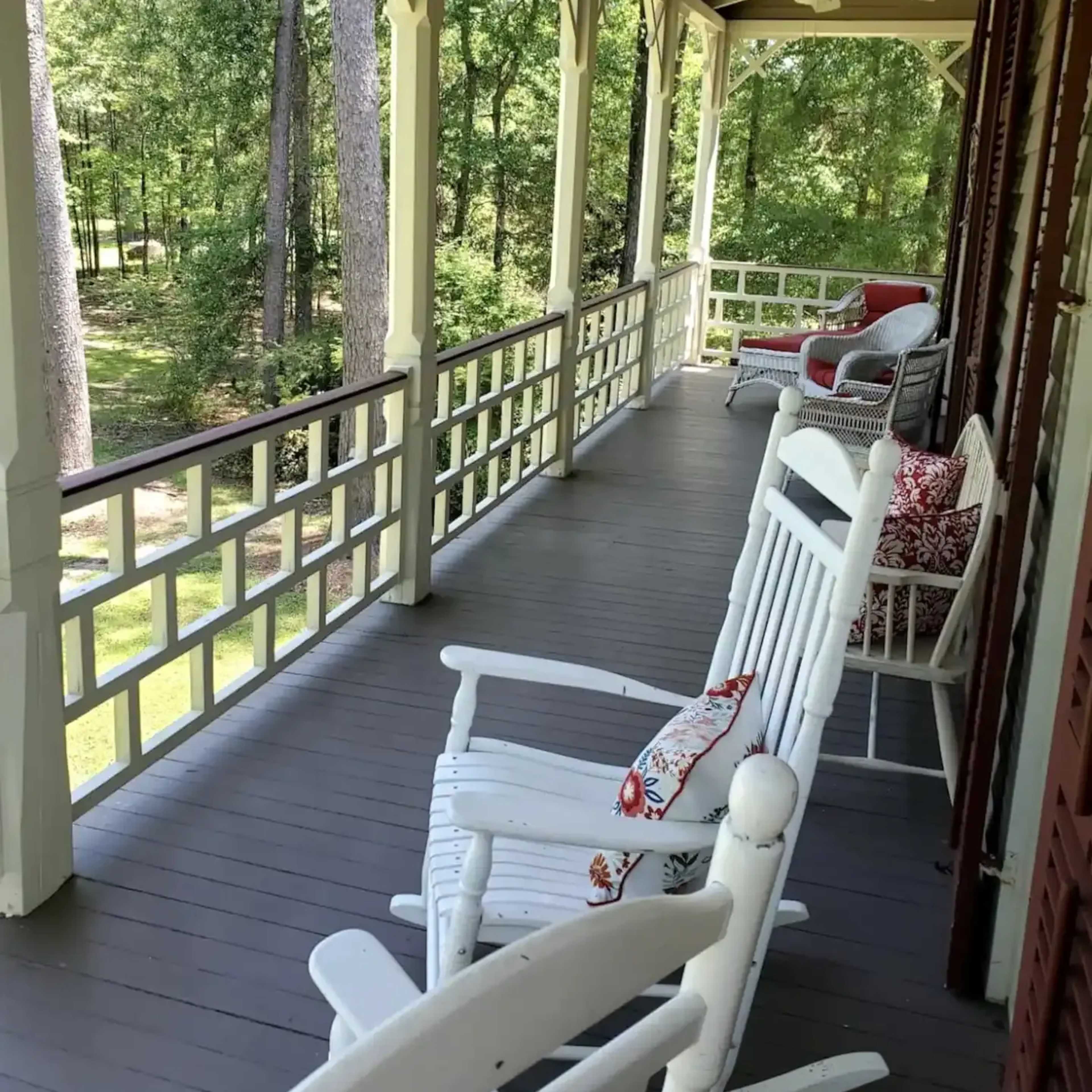 A covered porch with rocking chairs and a view of trees in the background.