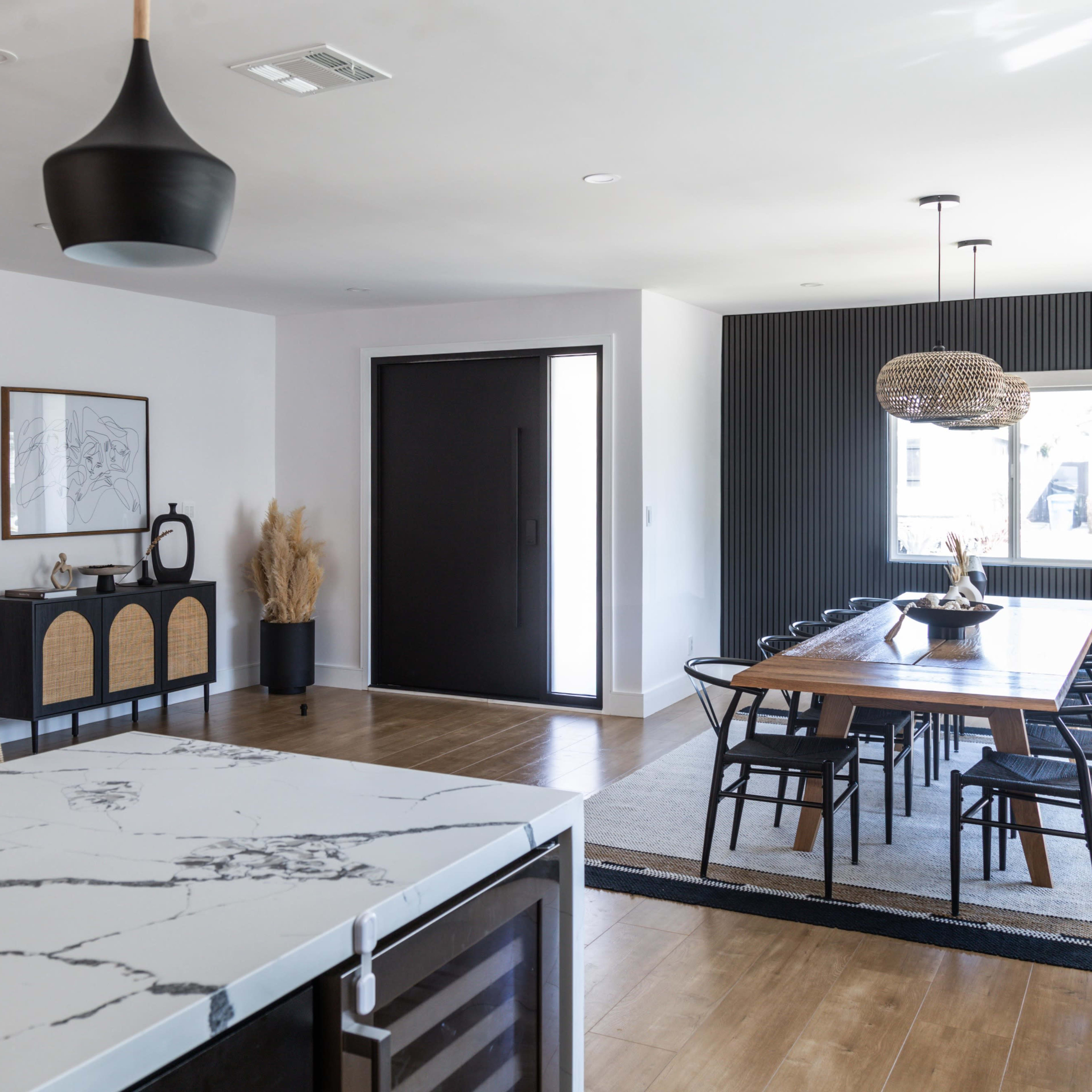 A modern interior features a dining area with a large wooden table, a kitchen island with a marble top, and a staircase leading to an upper level.