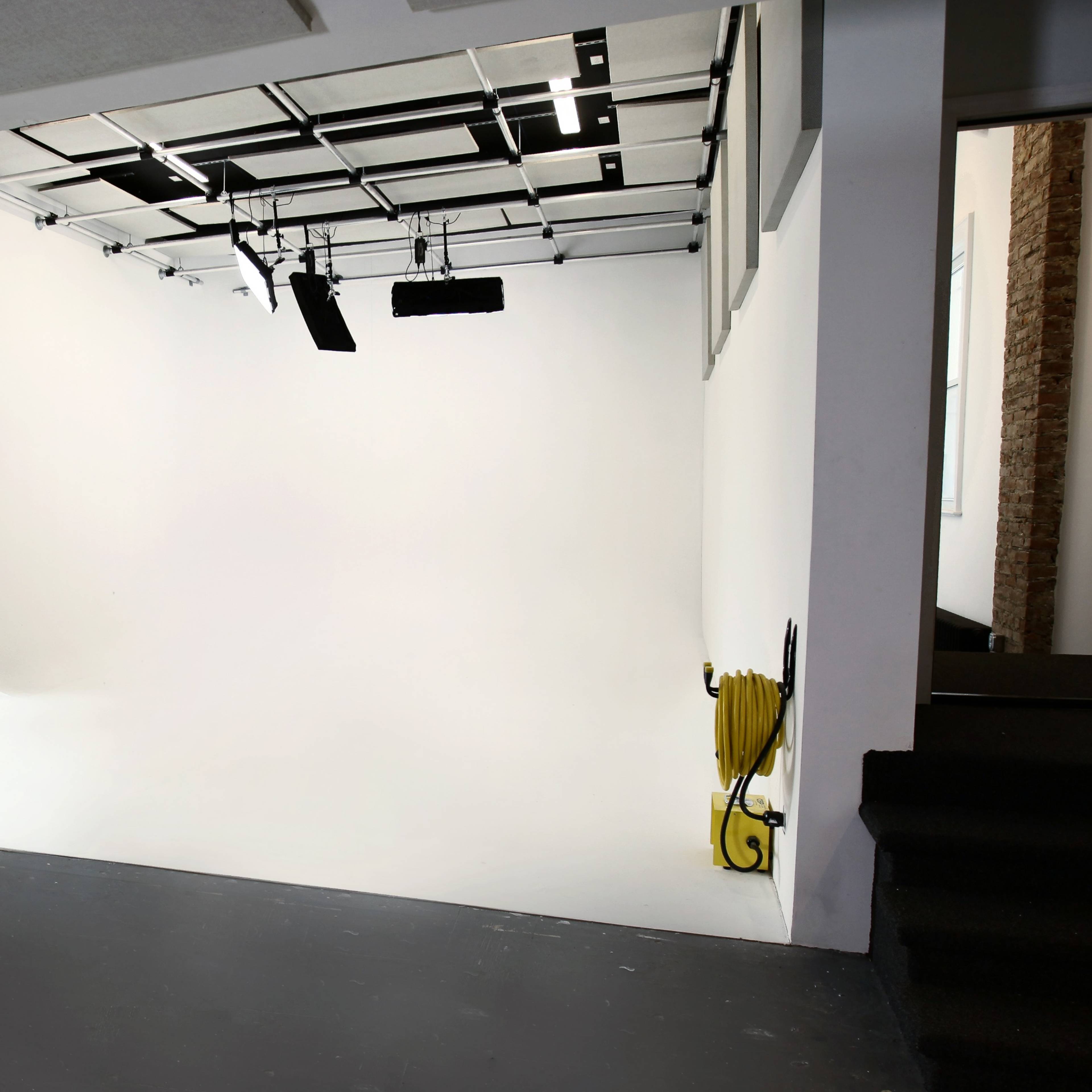 A blank, white studio space with industrial lighting and yellow cables on the floor.