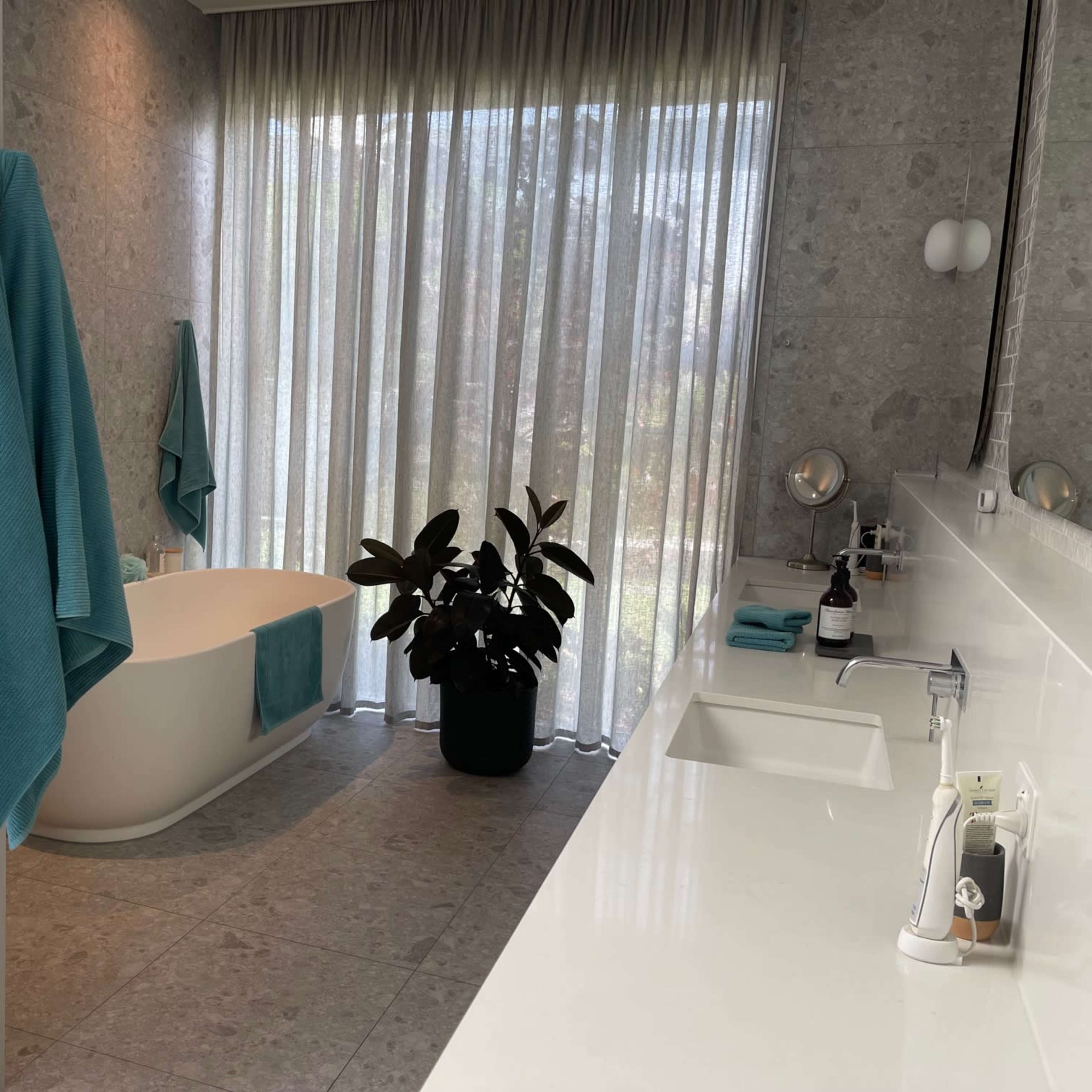 A modern bathroom featuring a freestanding tub, a plant in a black pot, and light blue towels hanging on the wall.