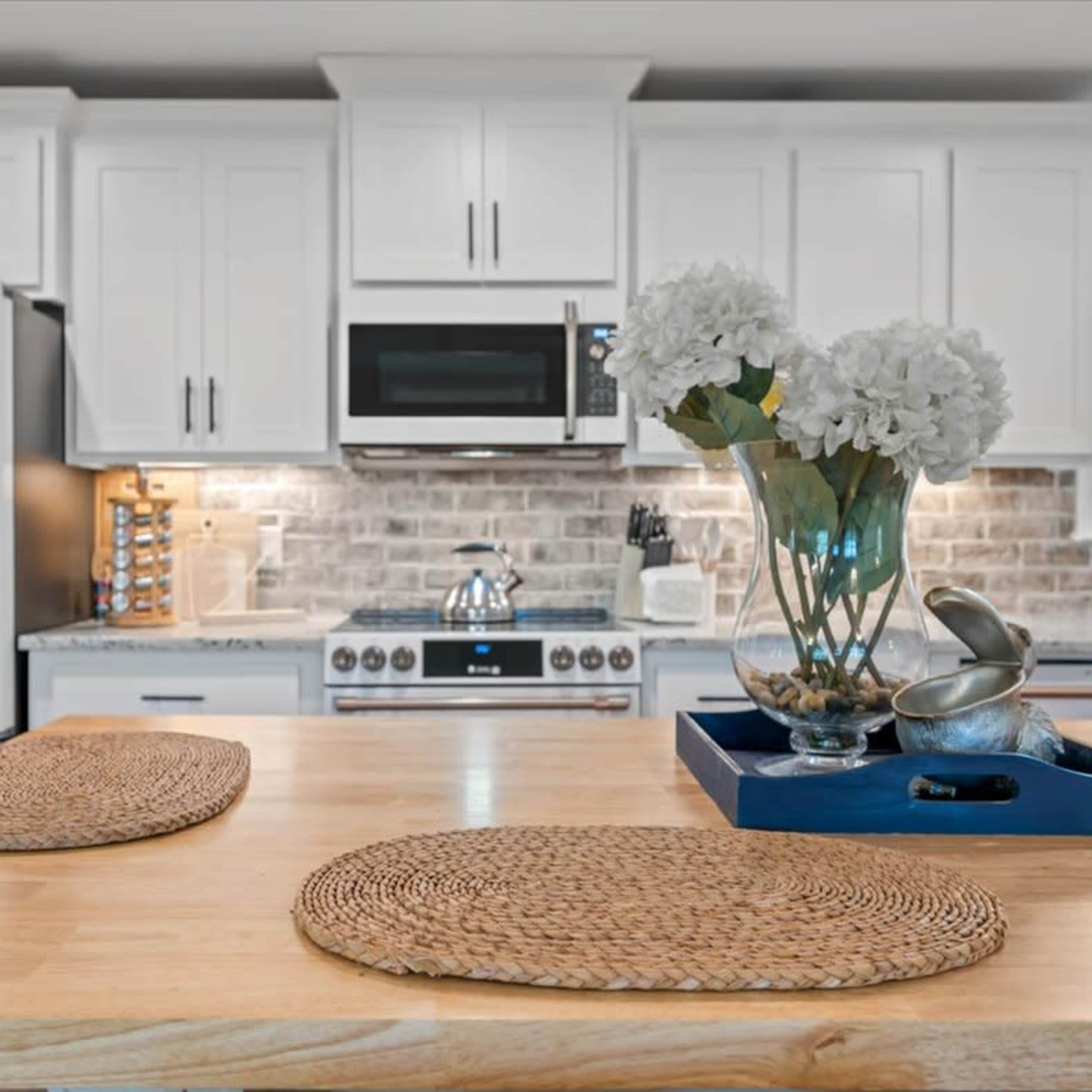 A modern kitchen features white cabinetry, stainless steel appliances, and a wooden dining table with woven placemats.