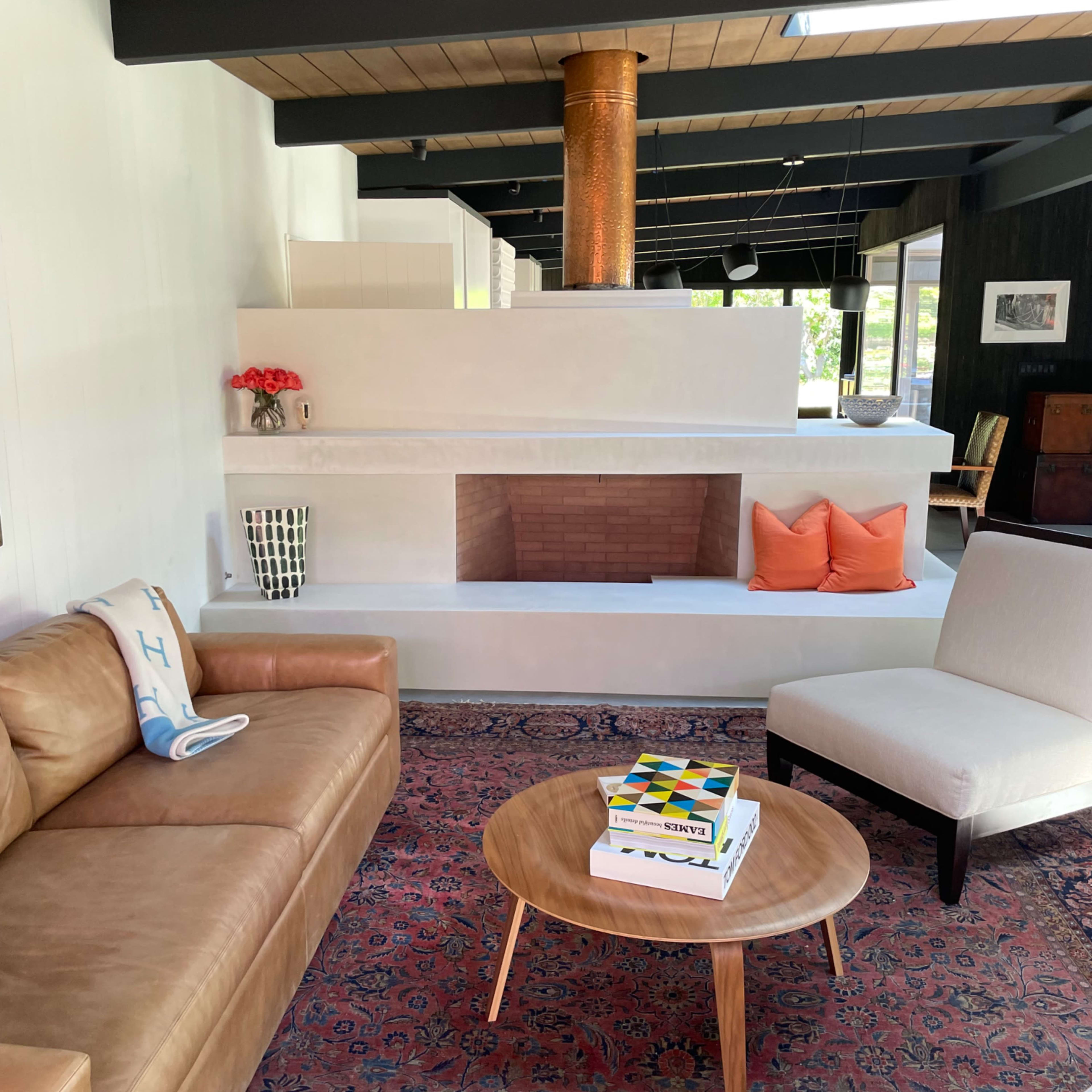 A modern living room with a leather sofa, an armchair, a round wooden coffee table, and a prominent fireplace featuring a copper flue.