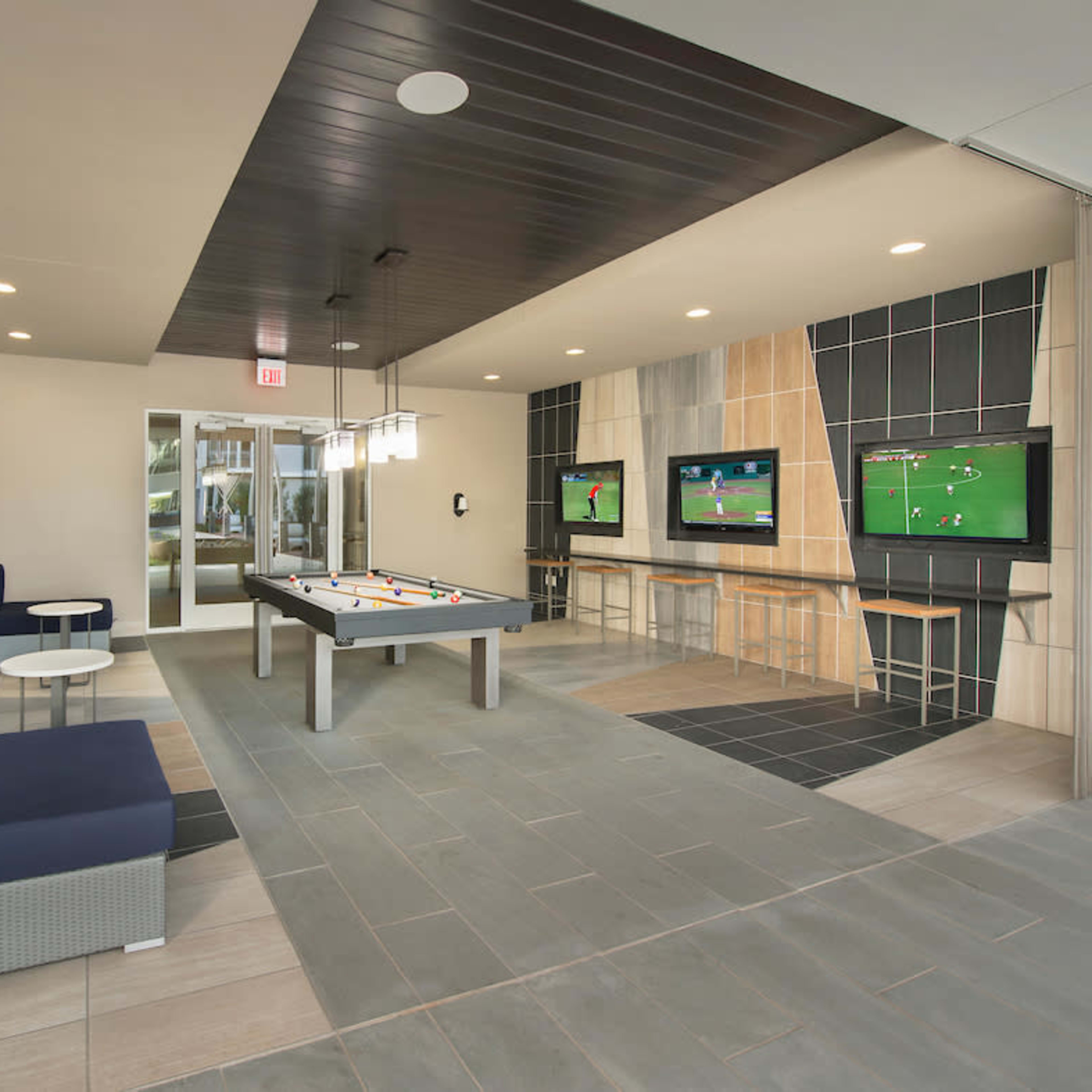 A modern lounge area featuring a pool table and two televisions mounted on the wall, surrounded by seating.