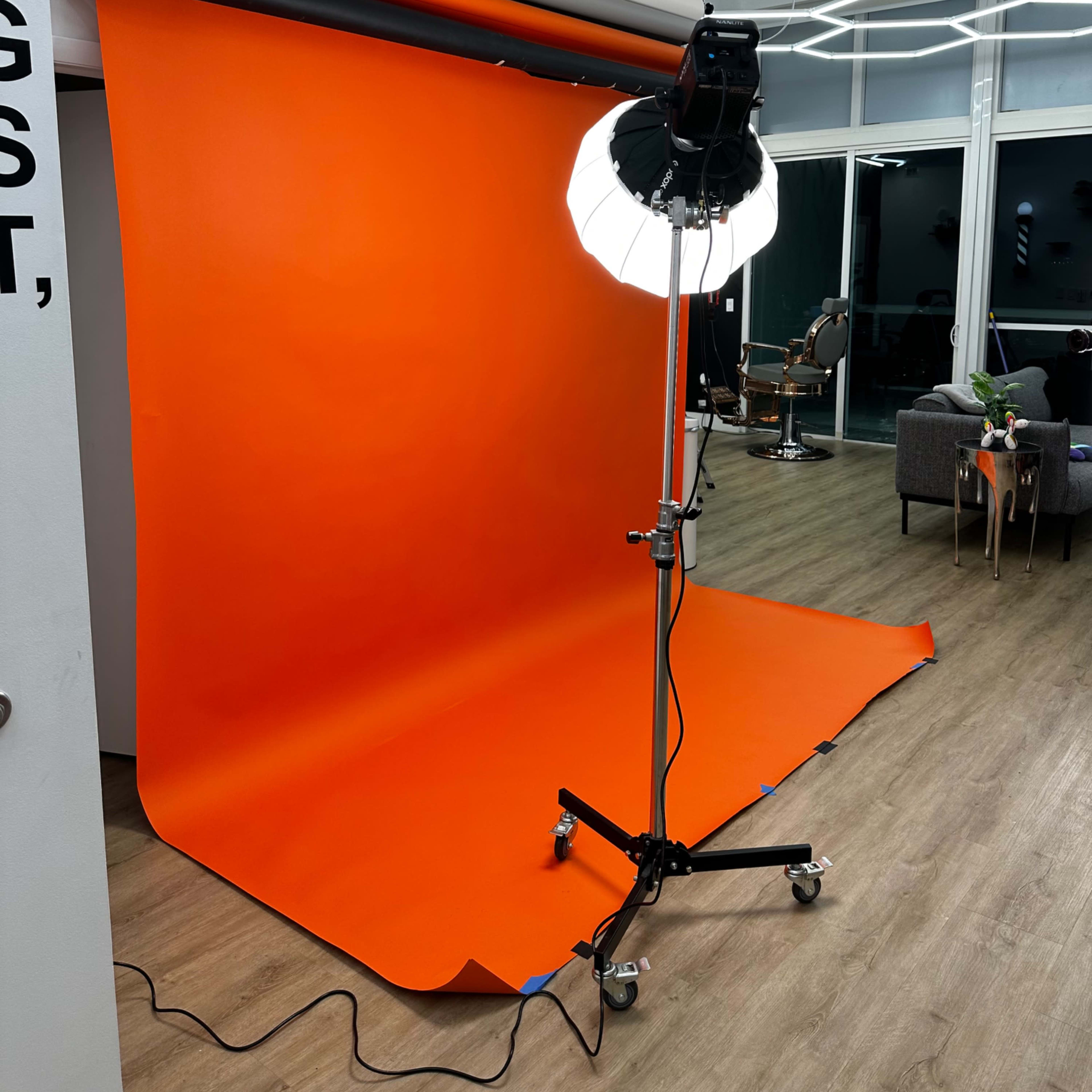 A photography studio with an orange backdrop, a lighting setup on a stand, and modern furnishings in the background.