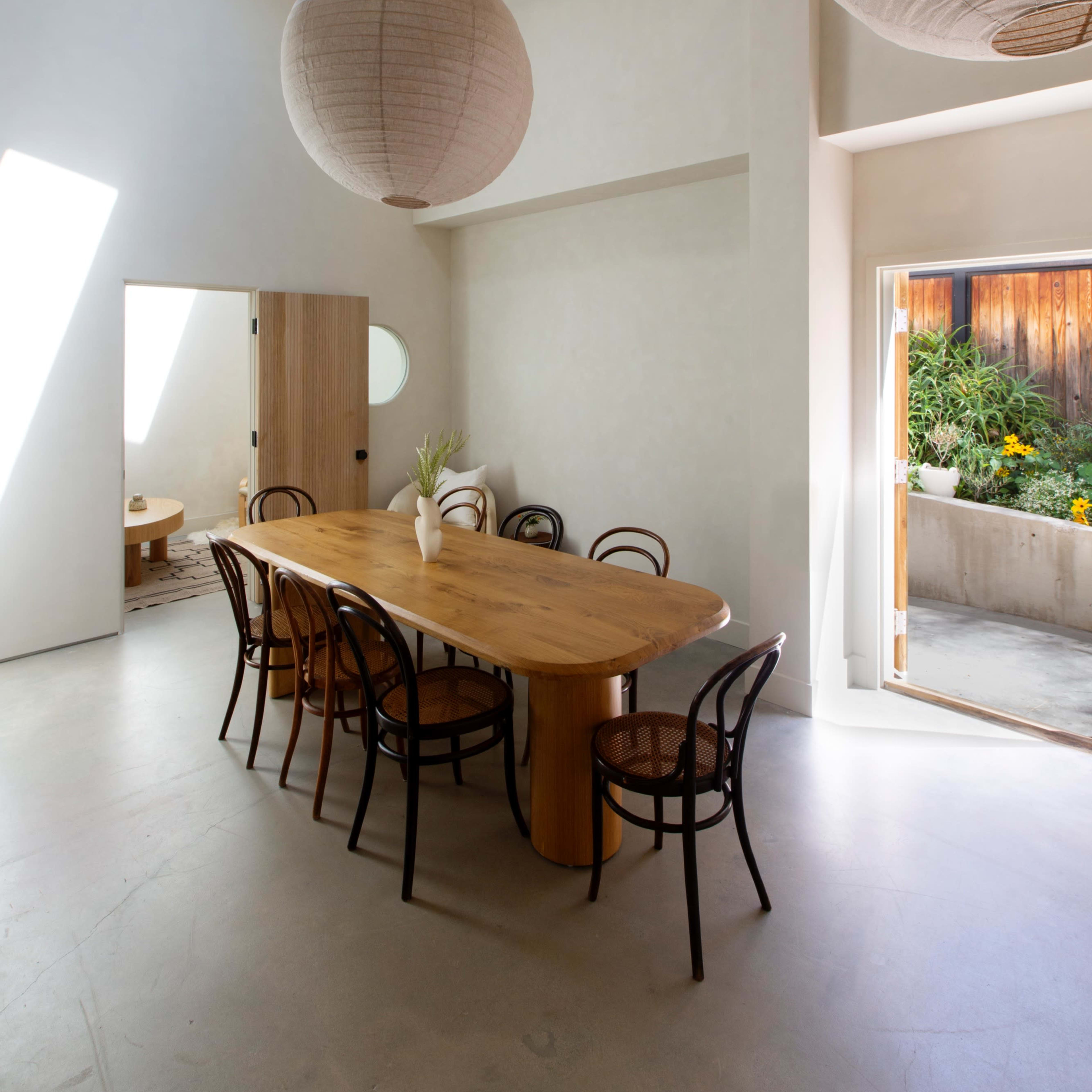 A spacious dining area features a large wooden table surrounded by curved chairs, illuminated by natural light from a skylight and large sliding door.