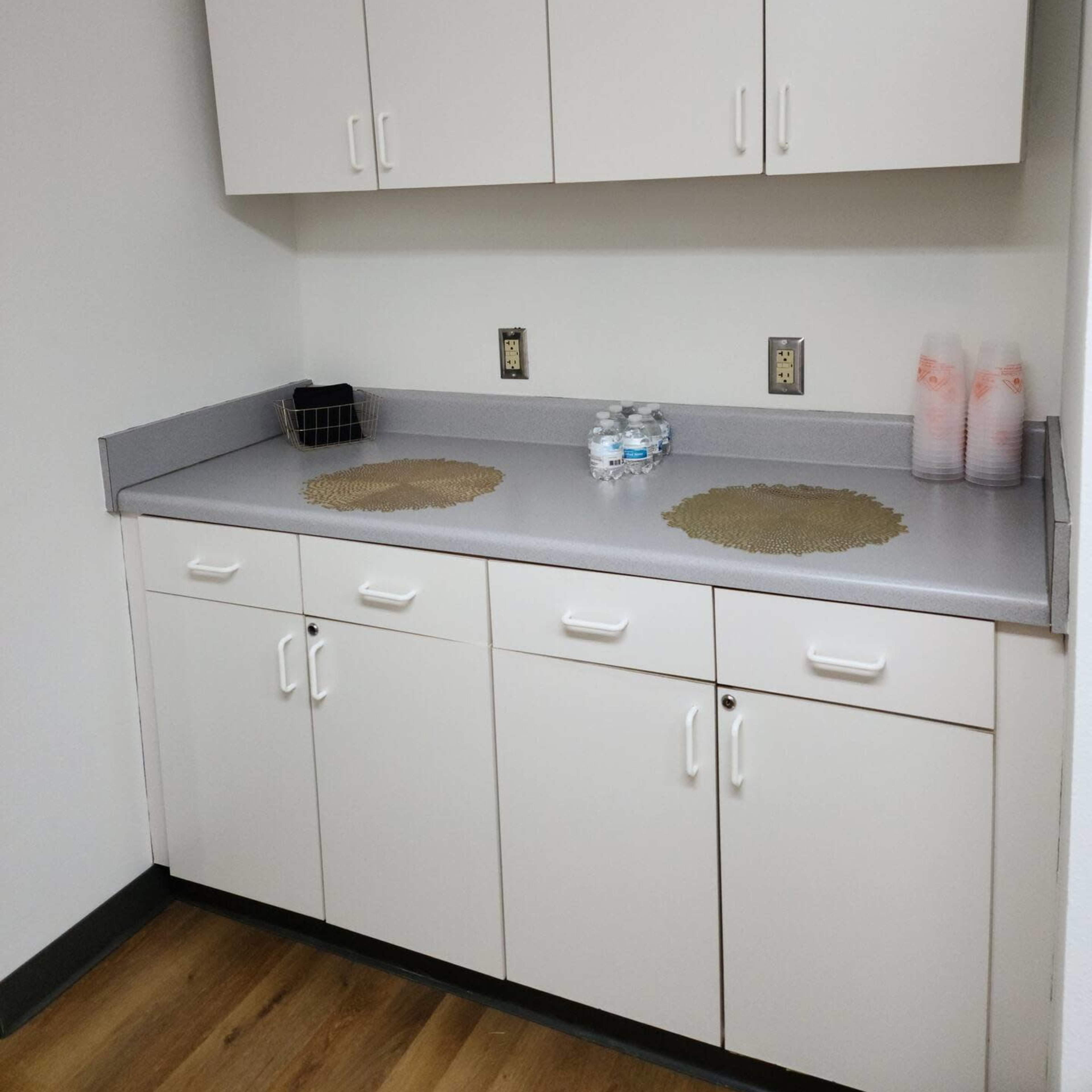 A small kitchen corner with white cabinetry, a countertop, and a few water bottles on the surface.