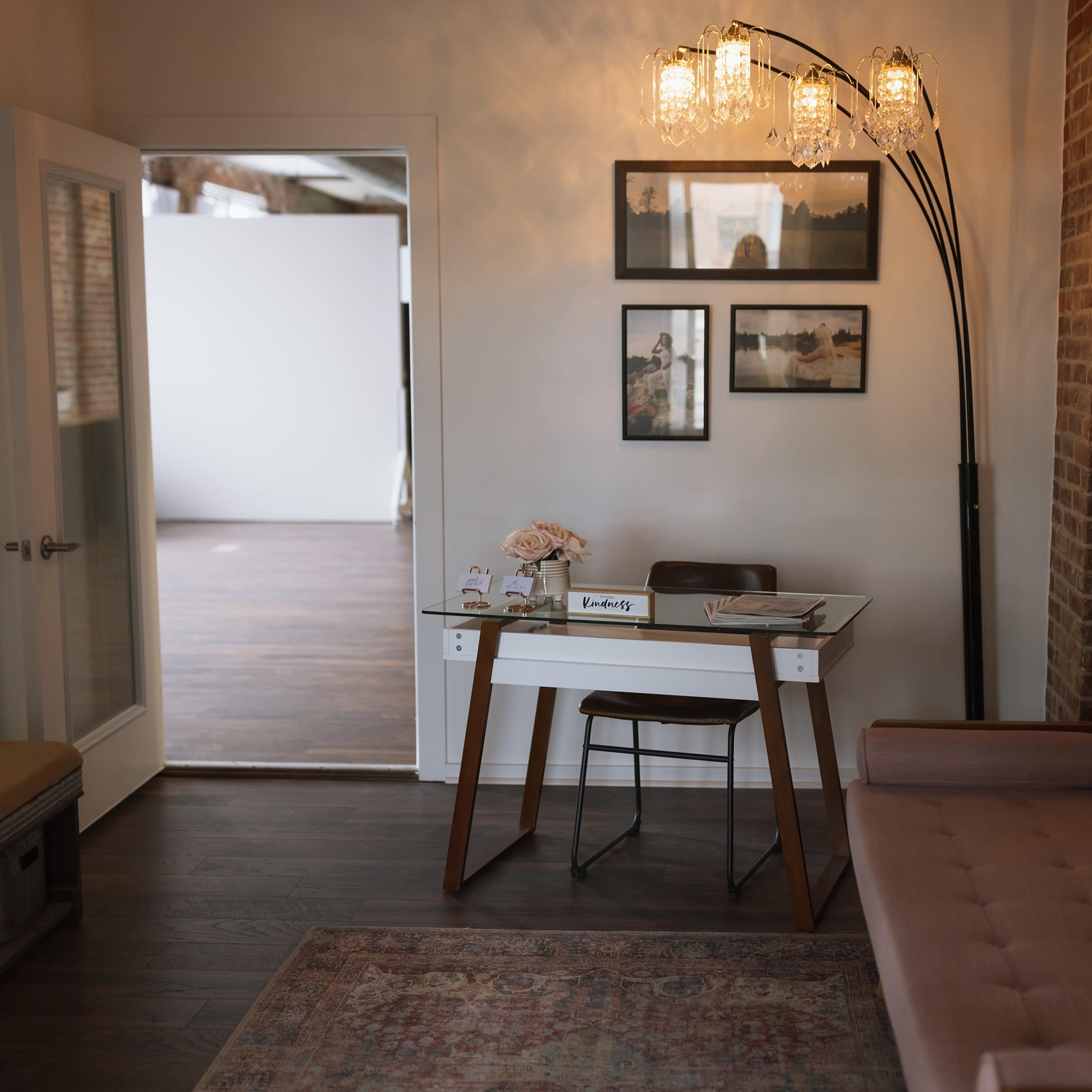 A row of white folding chairs is arranged in front of large windows in a room with exposed brick walls.