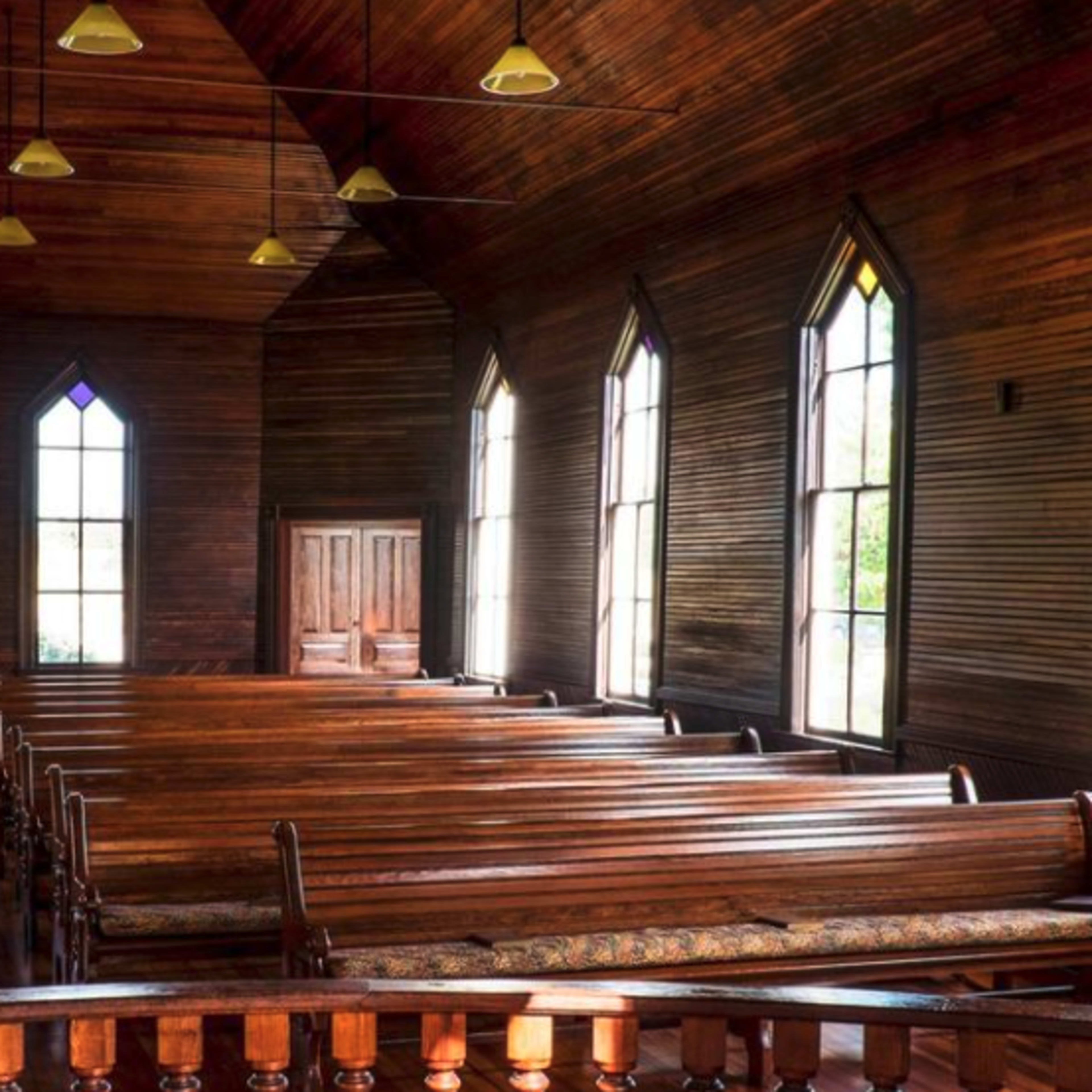 The interior of a wooden church features rows of pews and large, arched windows with stained glass.