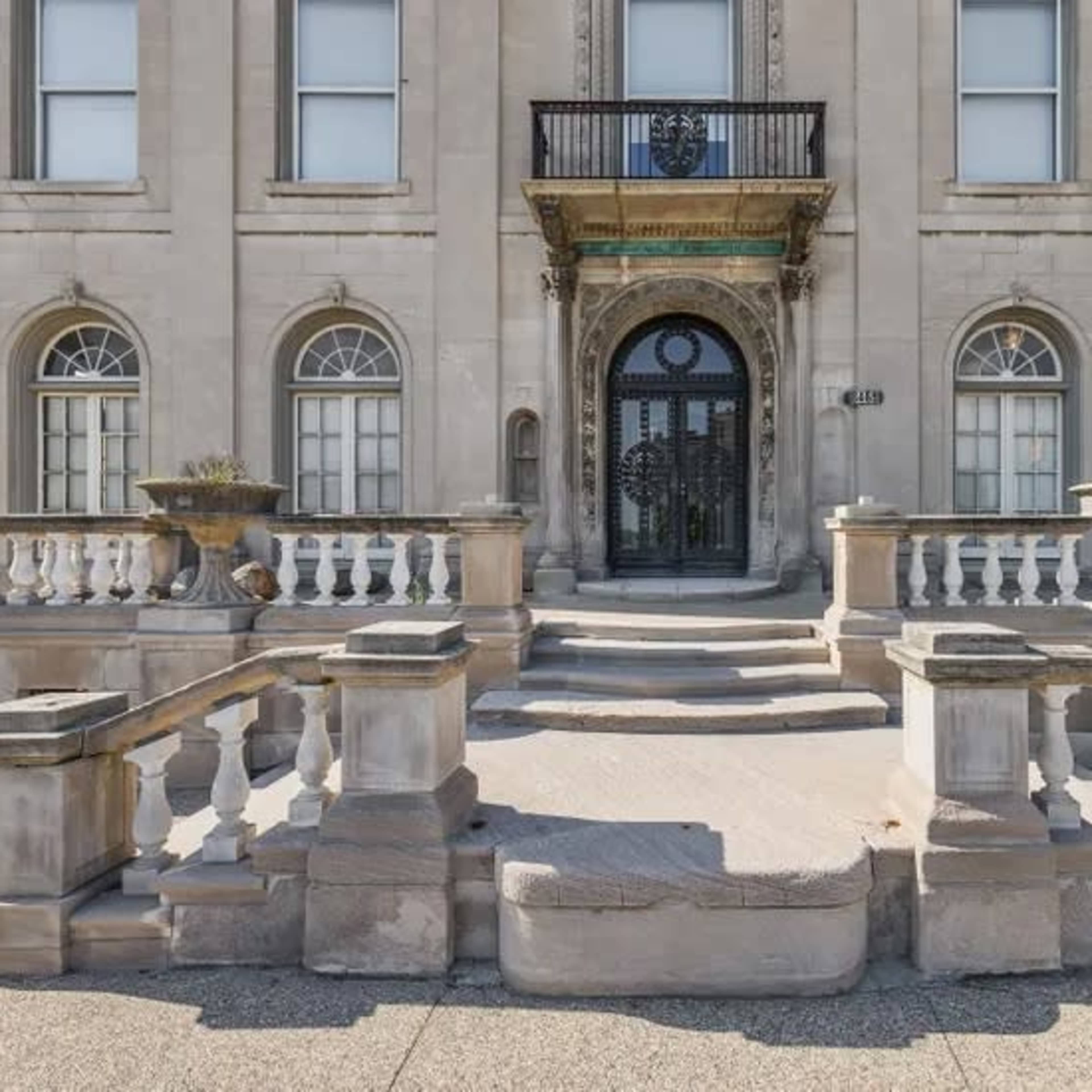 The grand entrance of a large stone building featuring a staircase with a railing and decorative planters on either side.