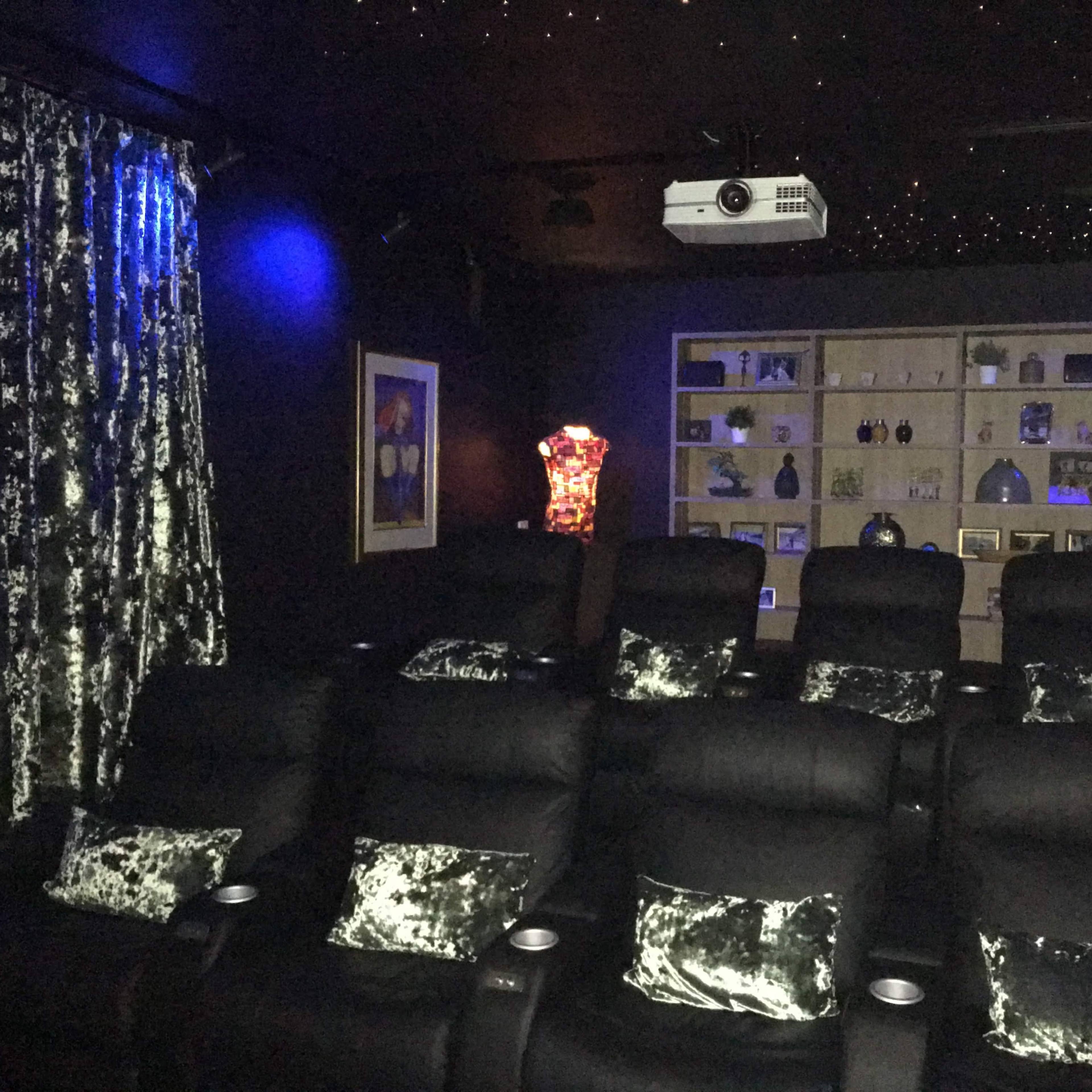 A home theater room with black recliner chairs, a projector, and a shelf displaying various decorative items.