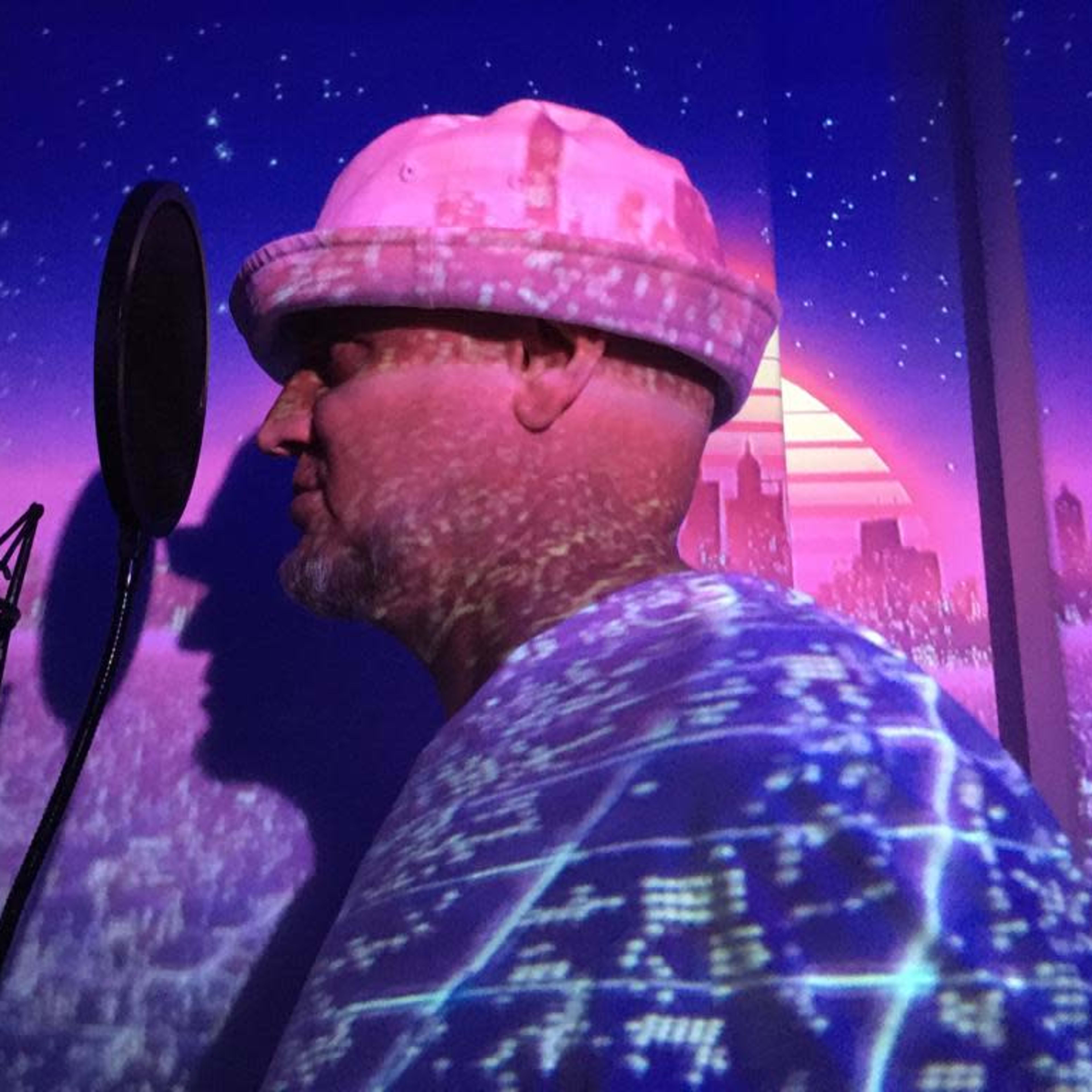 A man stands beside a microphone with a colorful cityscape projected onto his shirt and the wall behind him.