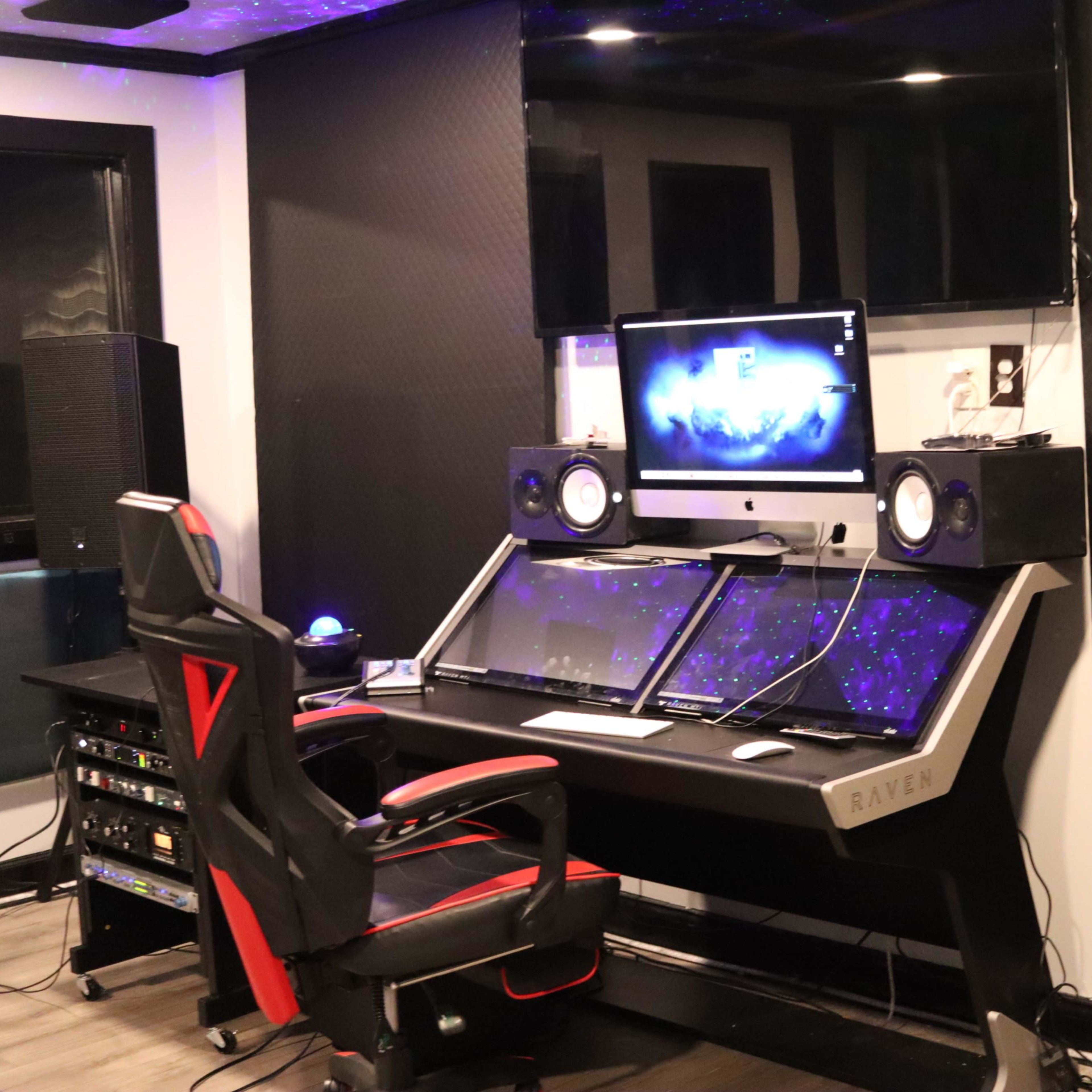 A modern music production studio with a sleek desk, dual monitors, studio speakers, and a black office chair.