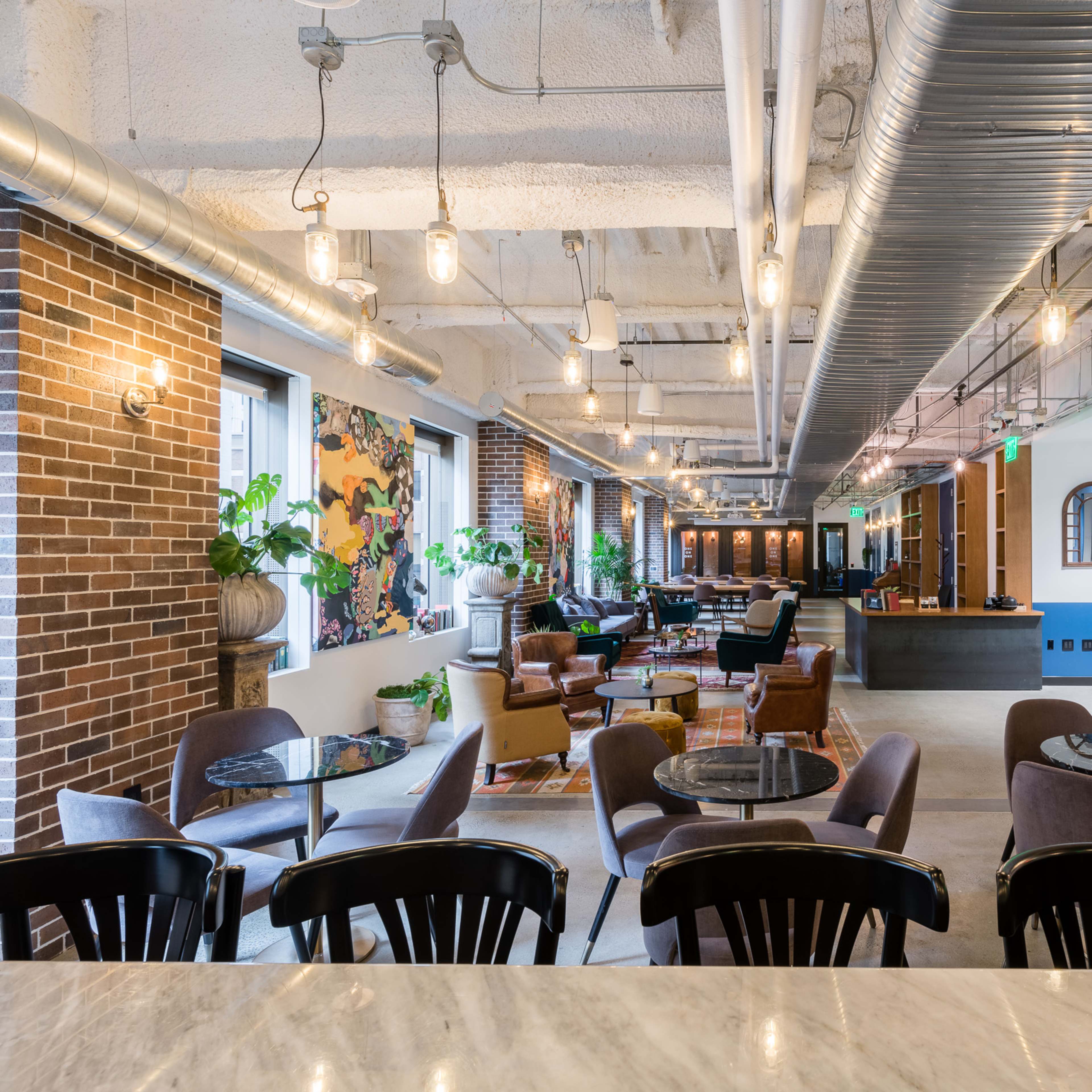 A modern open-concept lounge area with a bar, seating arrangements, and greenery in a well-lit space.