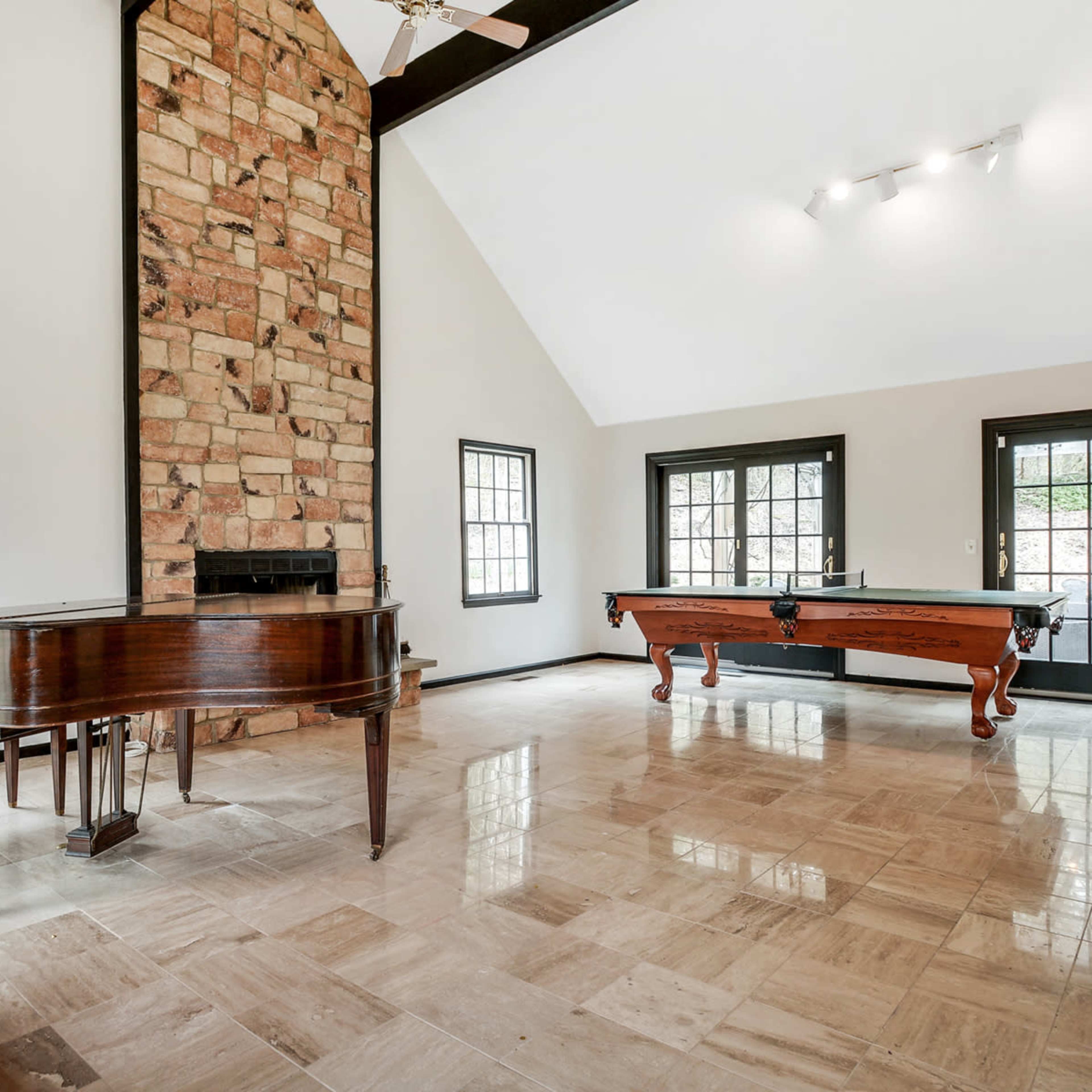 A spacious living area features a grand piano and a billiard table, flanked by large windows and a stone fireplace.