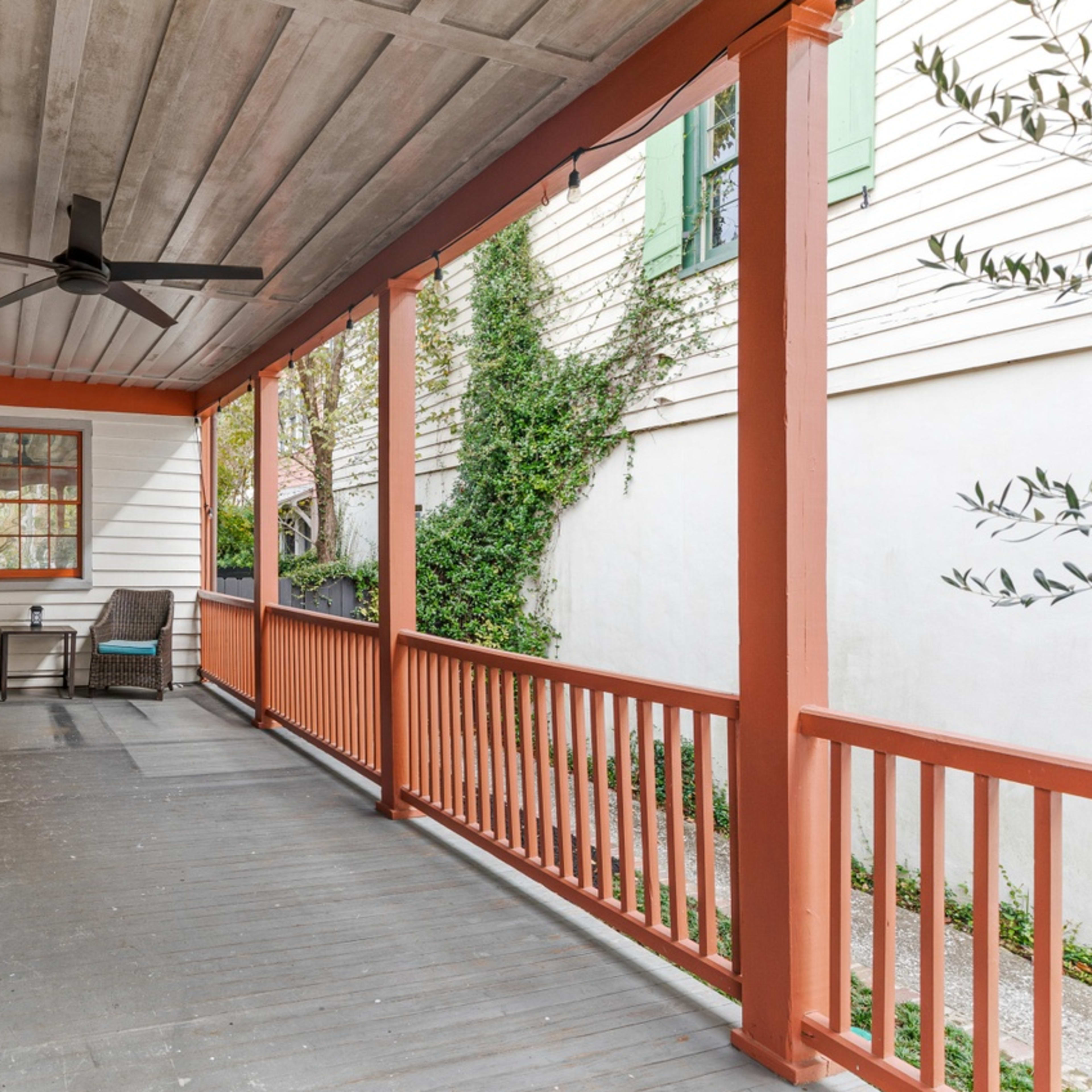 A covered porch with a ceiling fan, two seating areas, and wooden railings painted in orange.