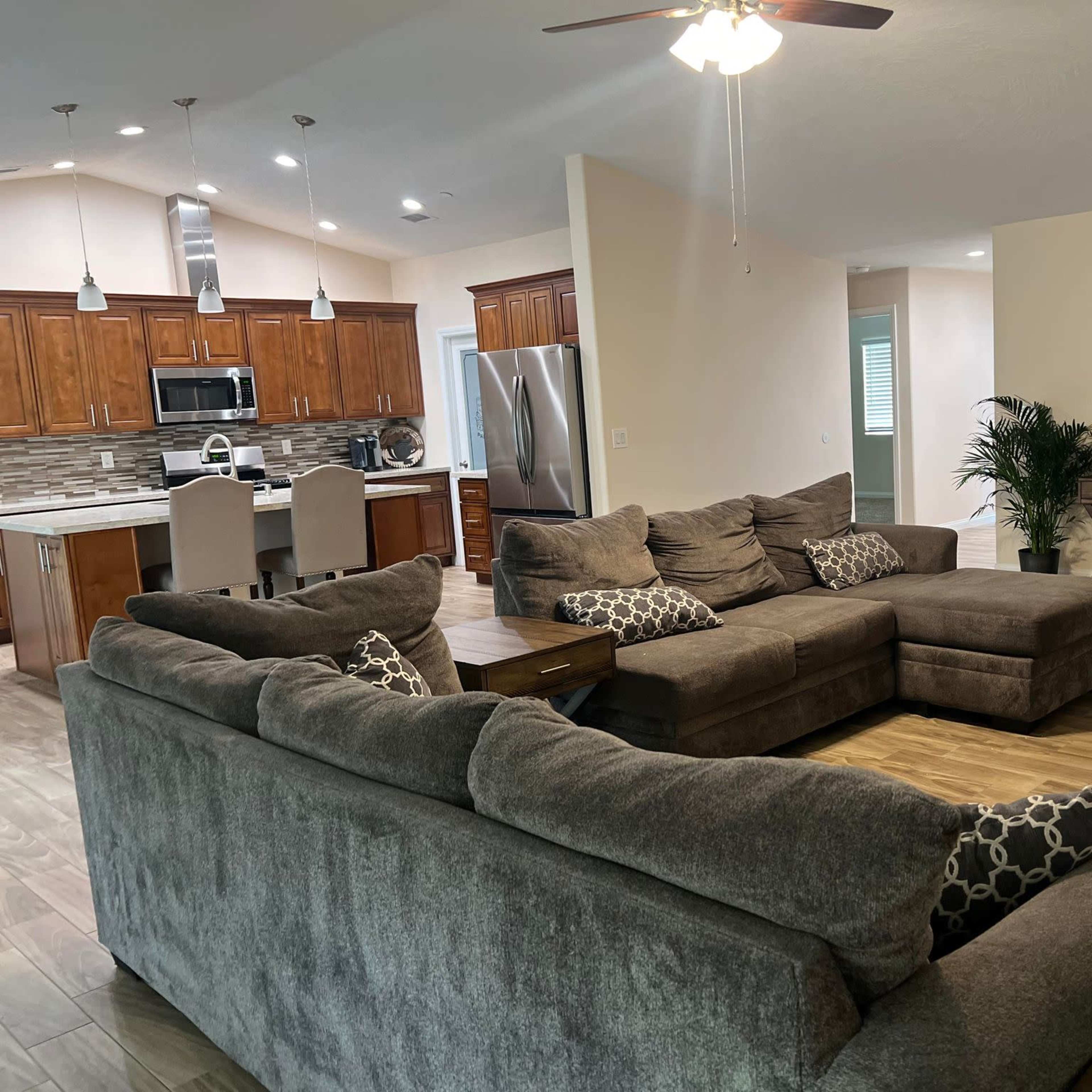 A spacious living area with a large sectional sofa, a coffee table, and a view of a modern kitchen in the background.