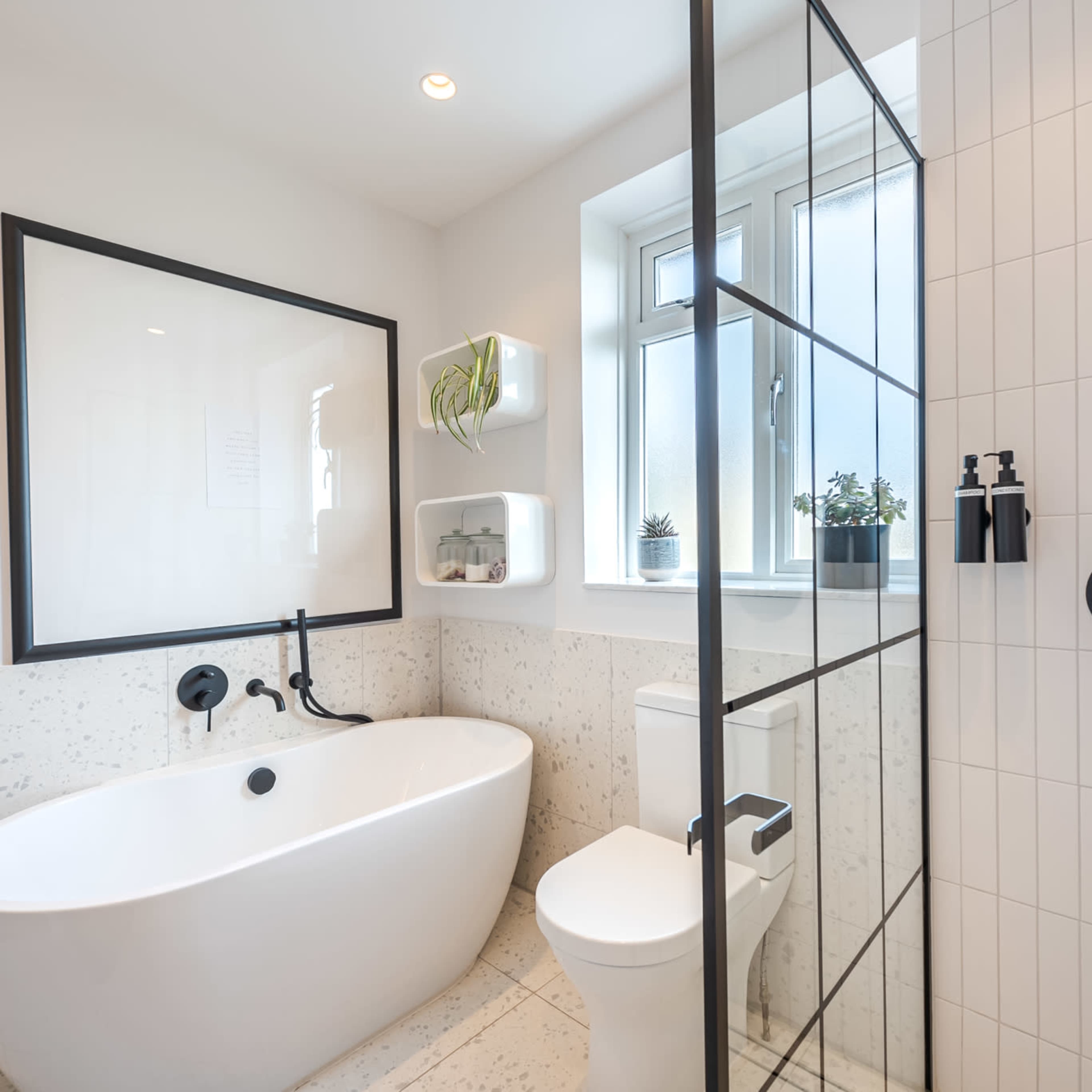 A modern bathroom featuring a freestanding bathtub, a glass shower enclosure, a toilet, and plants on the wall shelf.