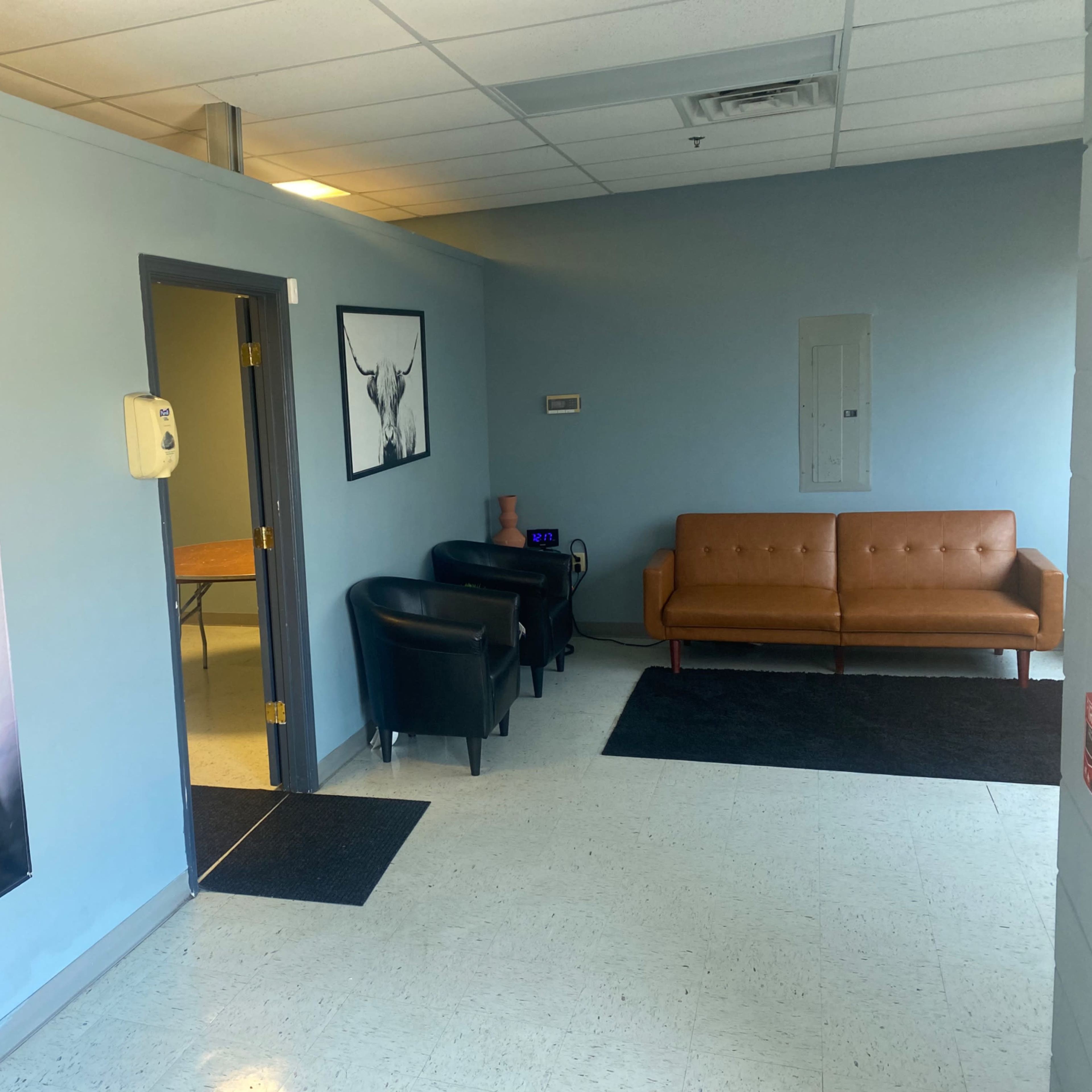 A waiting area with a brown couch, black chairs, and equine-themed wall art in a light blue room.