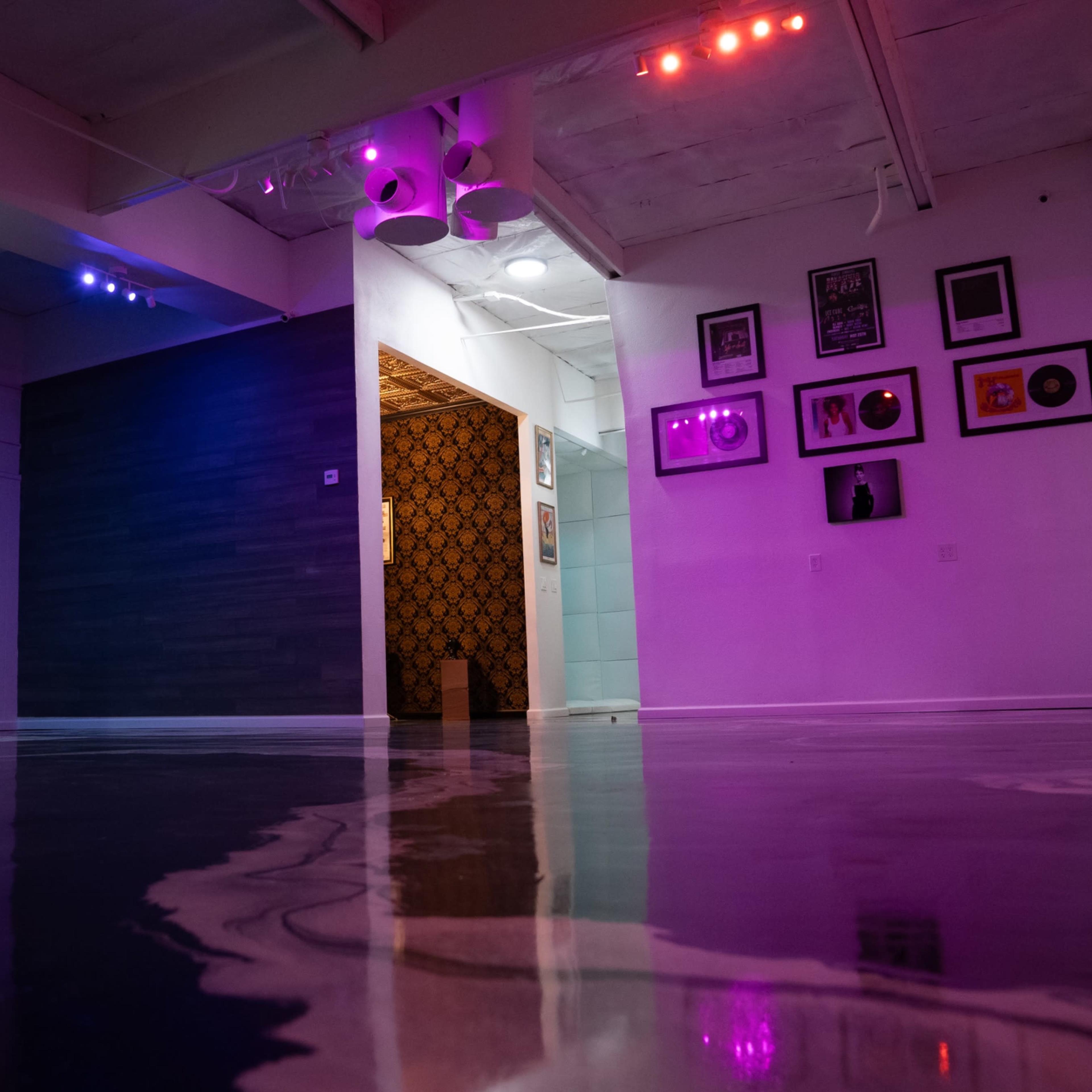 A spacious room with a glossy floor, featuring colorful lighting and a distinct wall with framed records and photos.