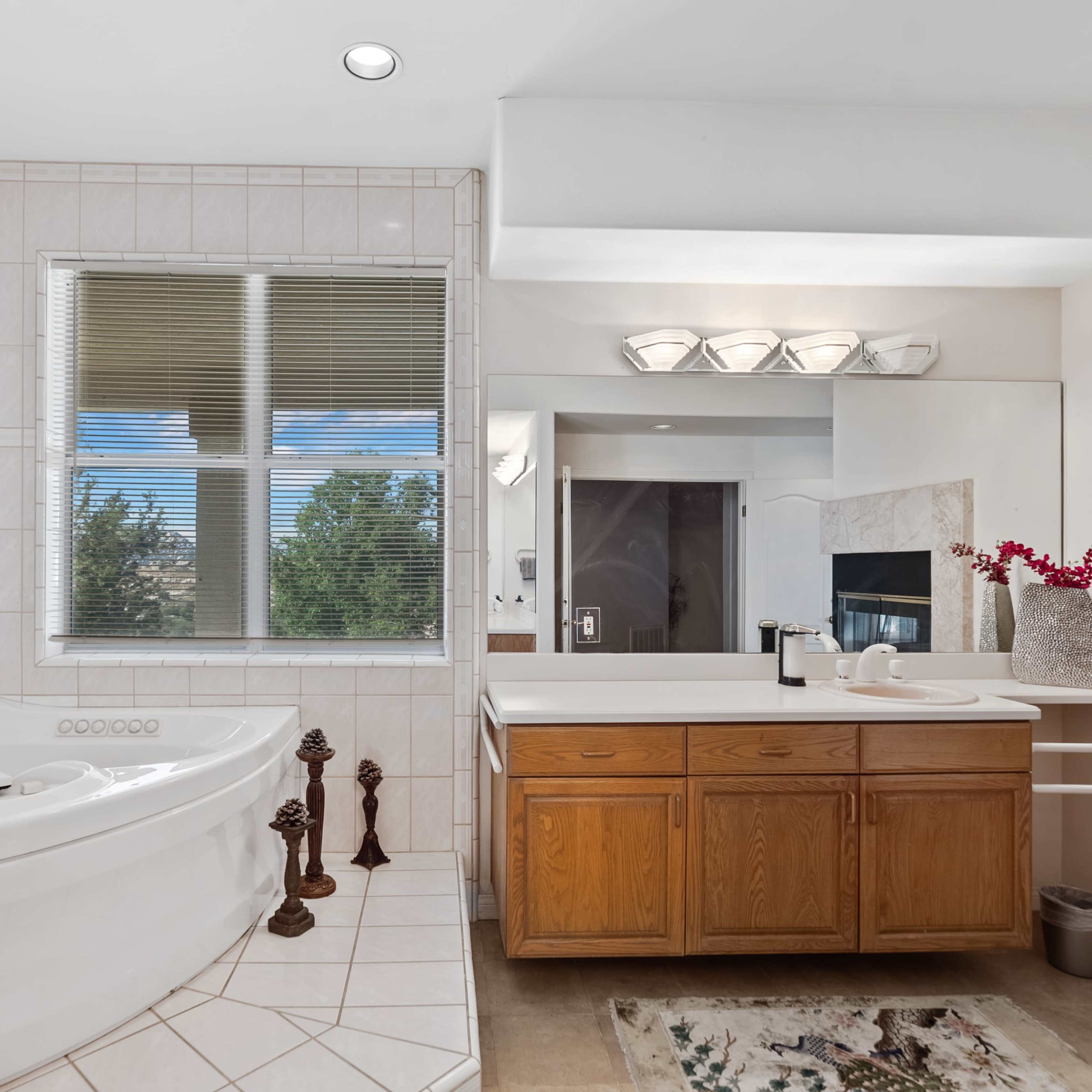 A bright bathroom features a large whirlpool bathtub, a double vanity with wooden cabinets, and a window providing natural light.