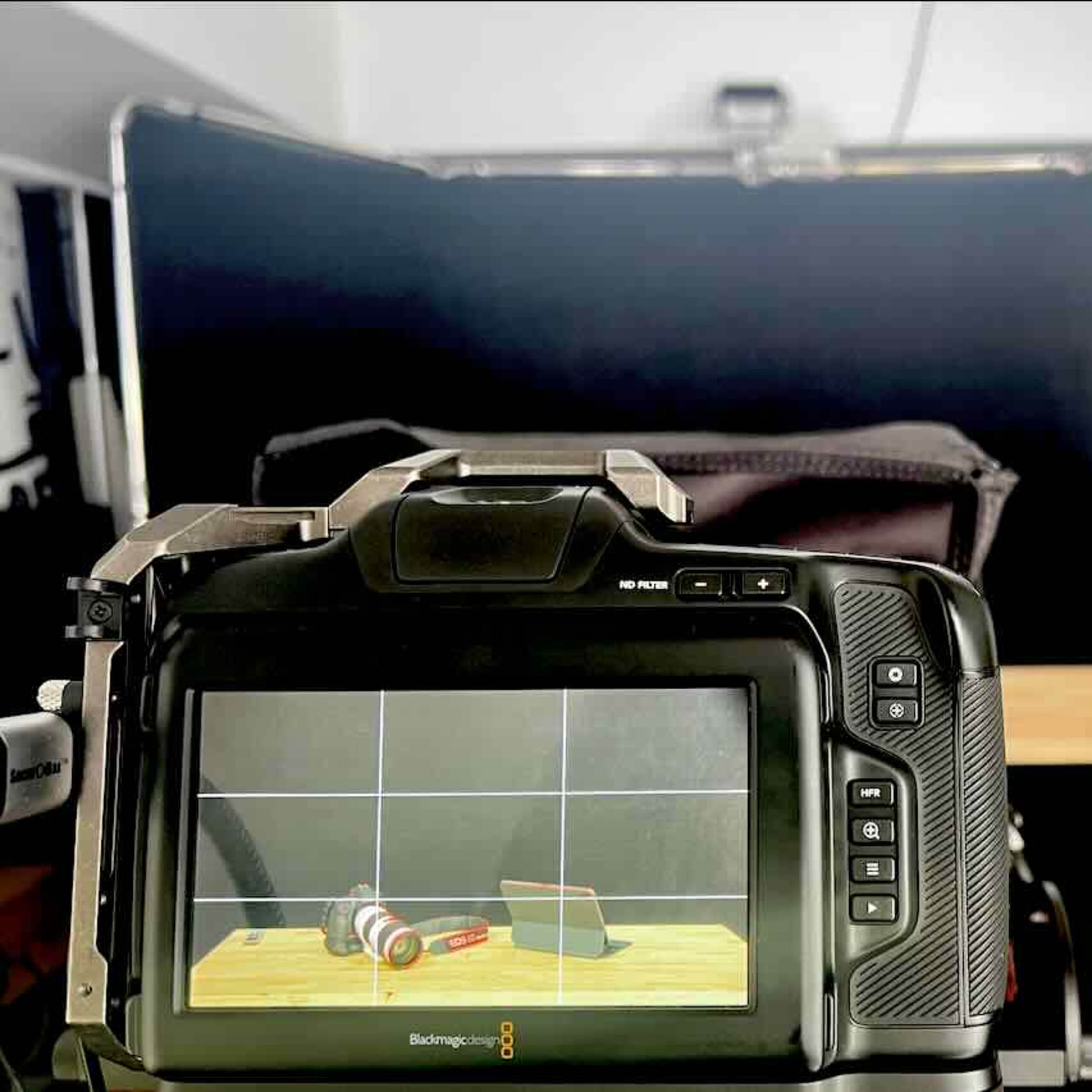 A camera is positioned in front of a black backdrop, displaying a setup featuring a camera lens and a book on a wooden table.
