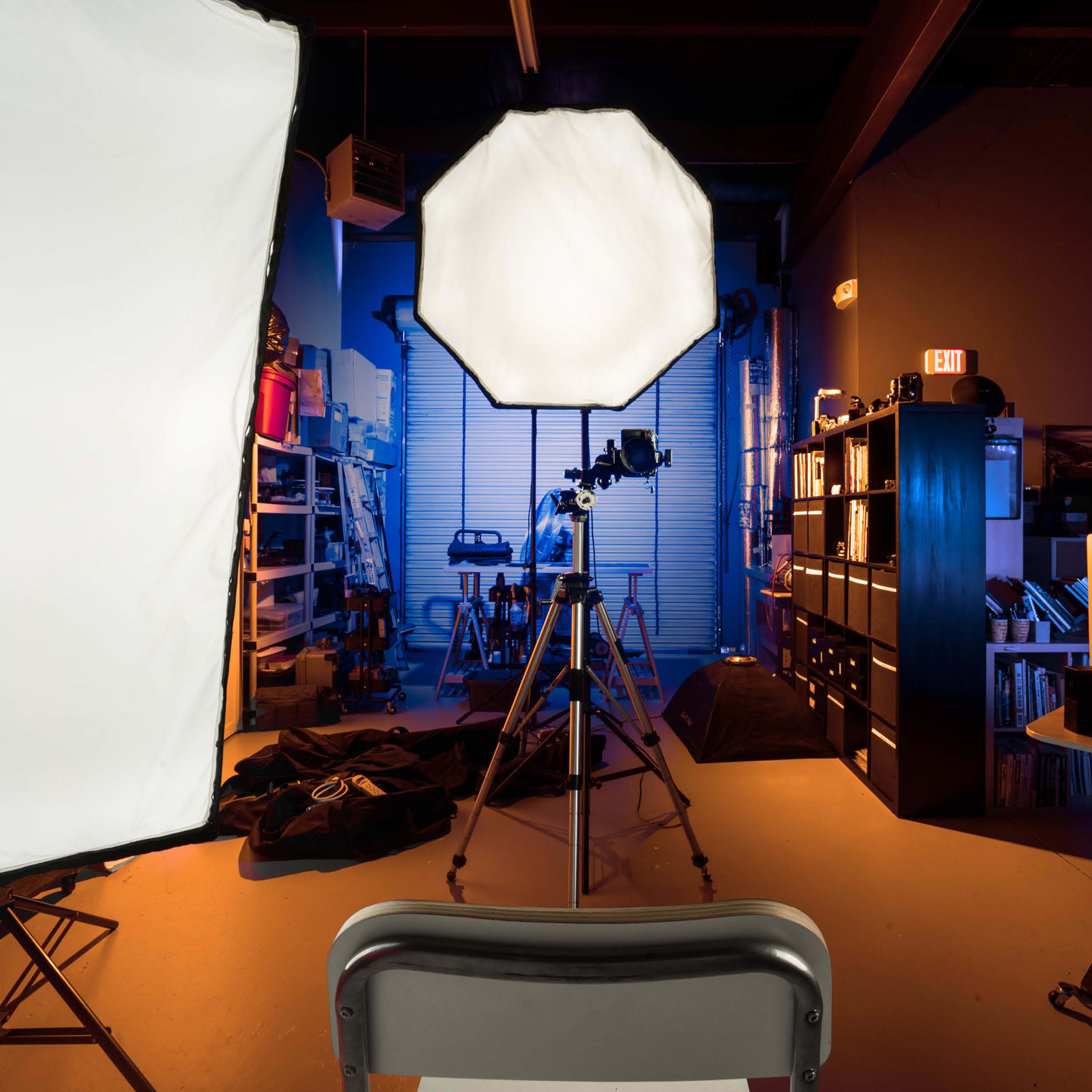 A photography studio setup with softbox lights, a camera on a tripod, and a backdrop in an organized workspace.