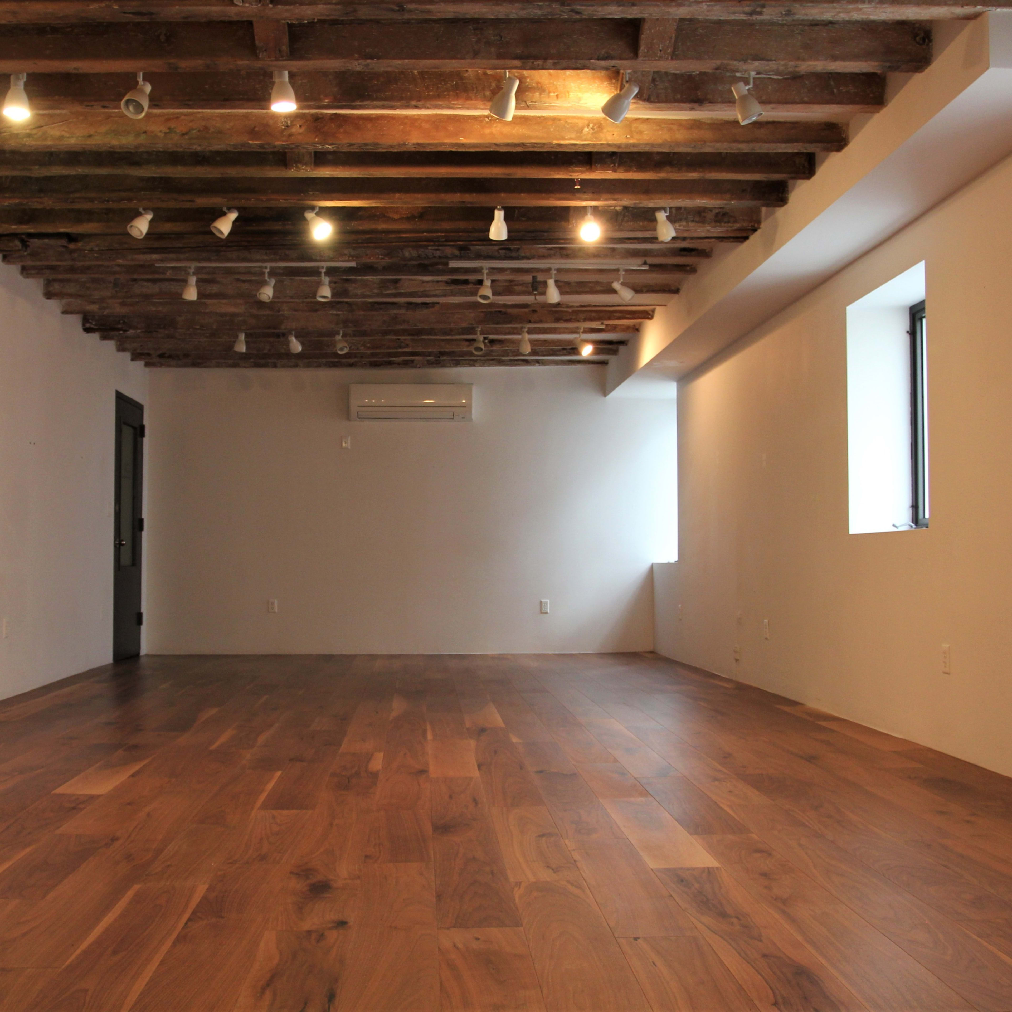 An empty room features wooden flooring, exposed beam ceilings, and two windows allowing natural light.