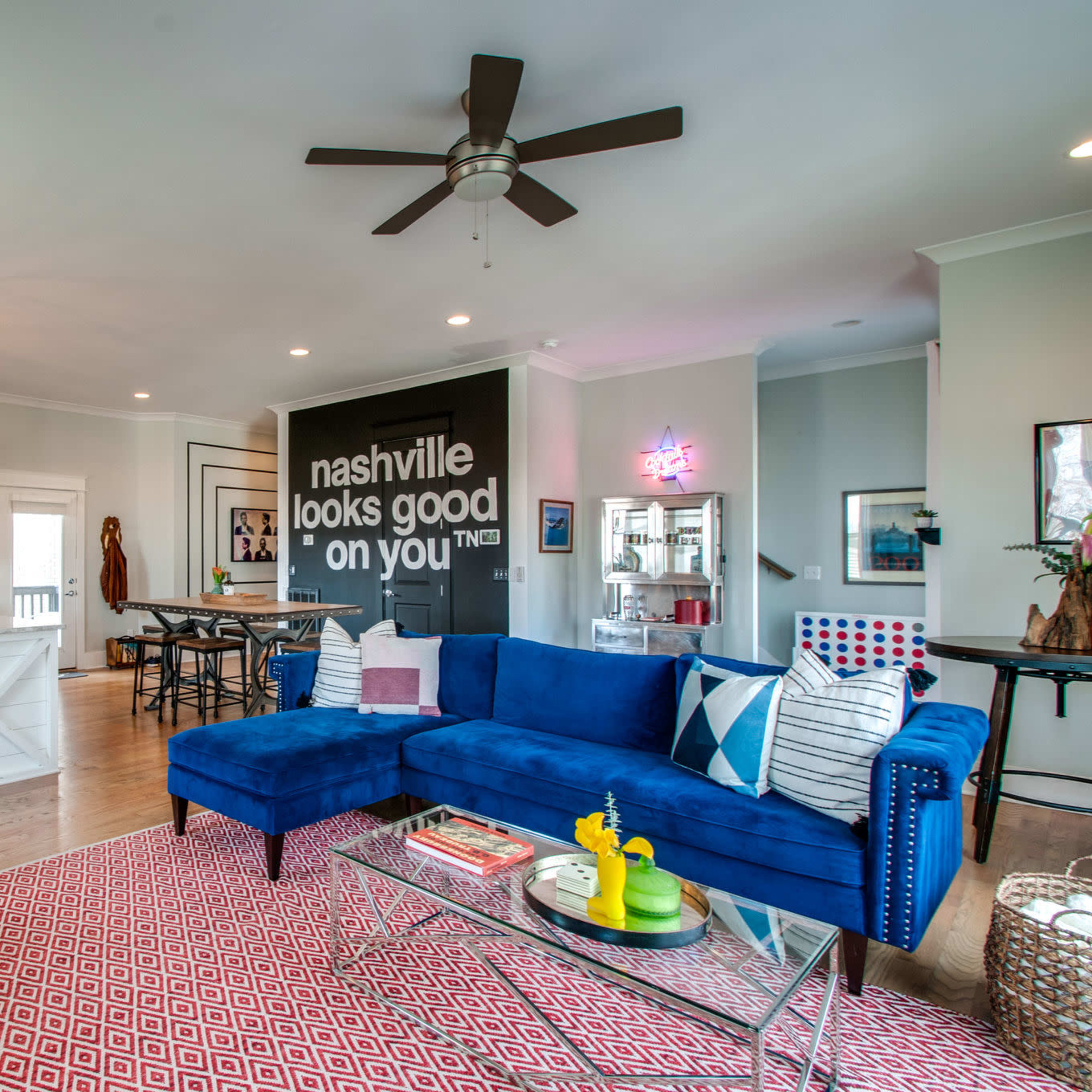 A modern living space featuring a blue sectional sofa, a dining area with a black table, and a kitchen with white cabinetry.