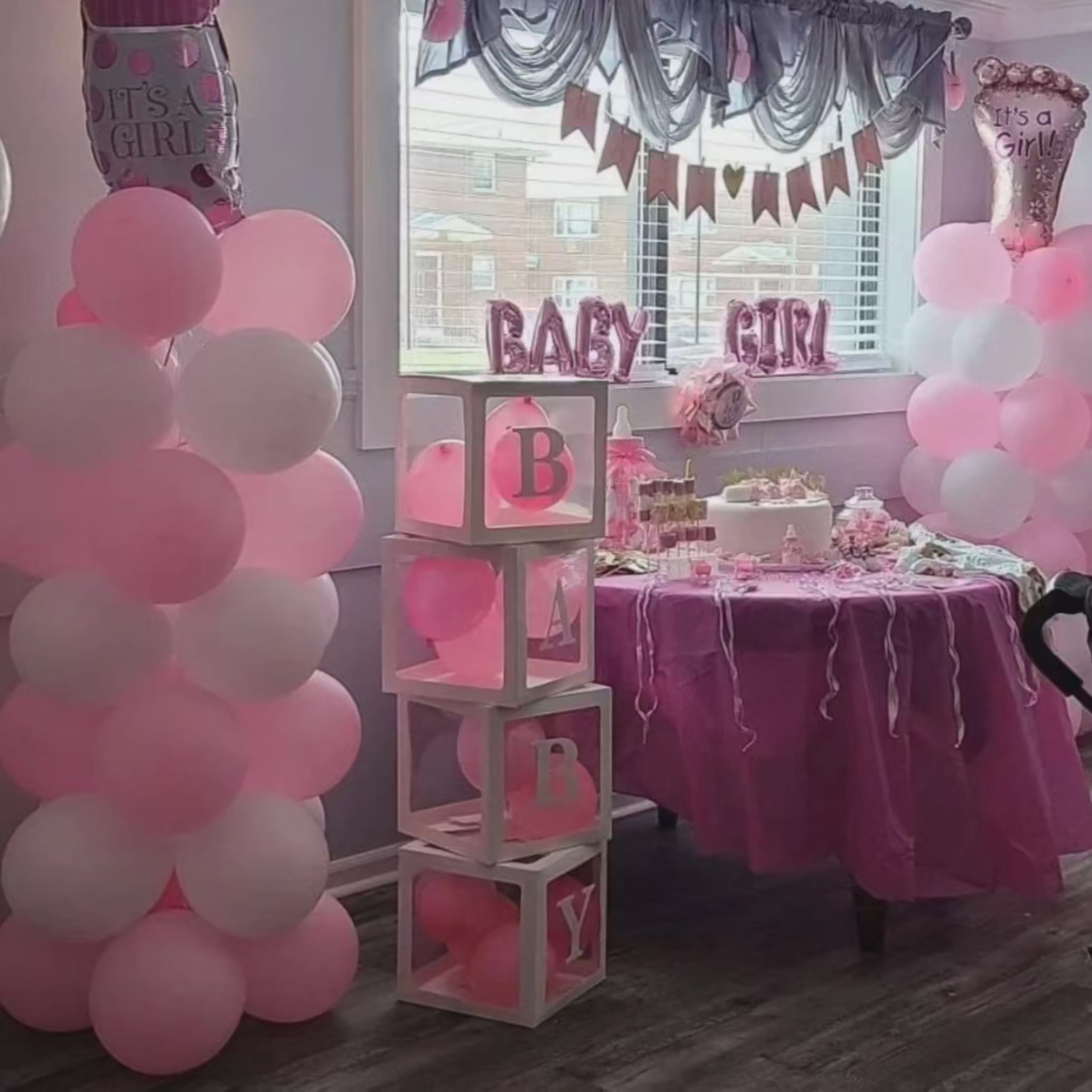 A decorated room for a baby girl celebration, featuring pink balloons, a dessert table with themed treats, and "BABY GIRL" letters displayed.