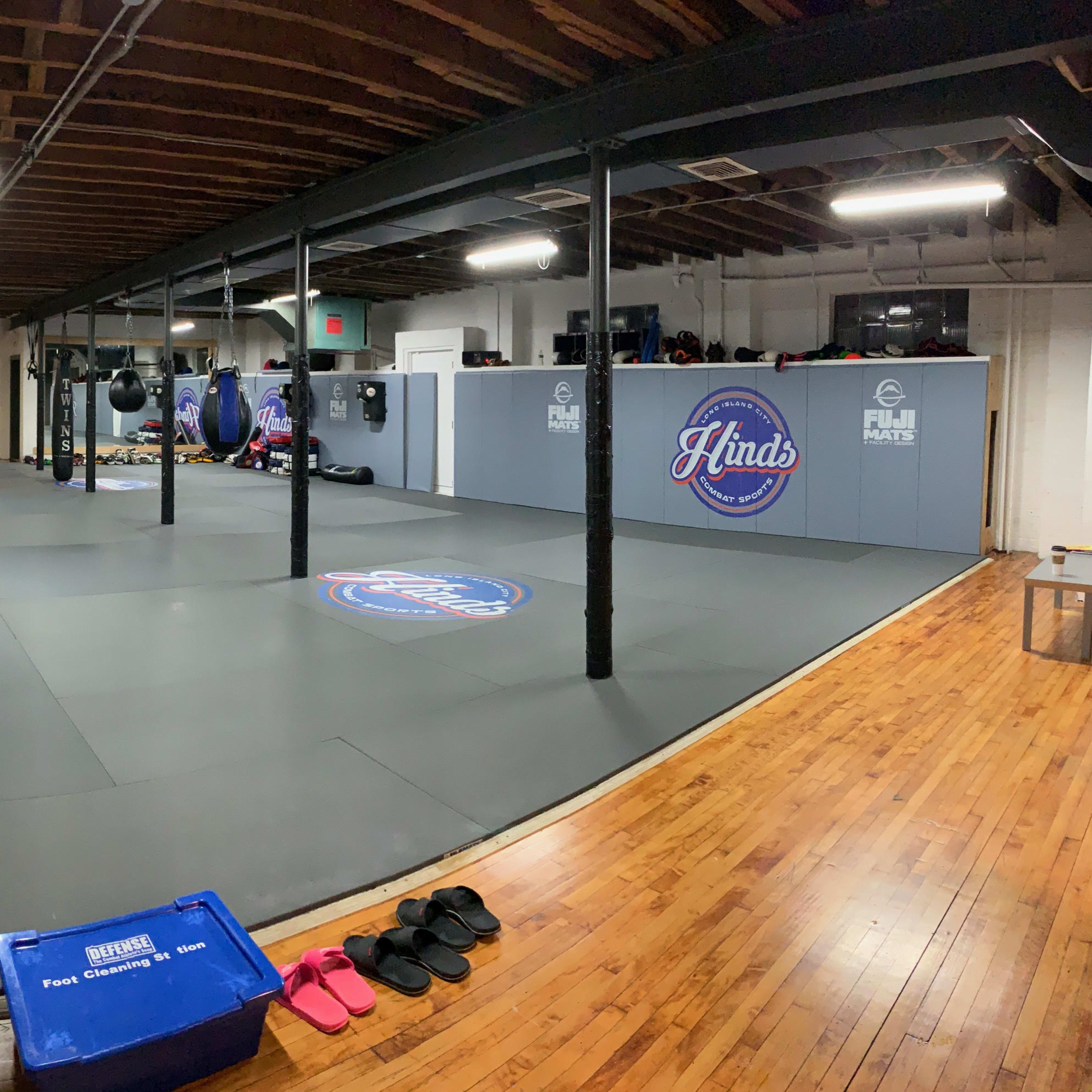 A spacious martial arts studio with padded flooring, hanging punching bags, and a centralized logo on the mat.