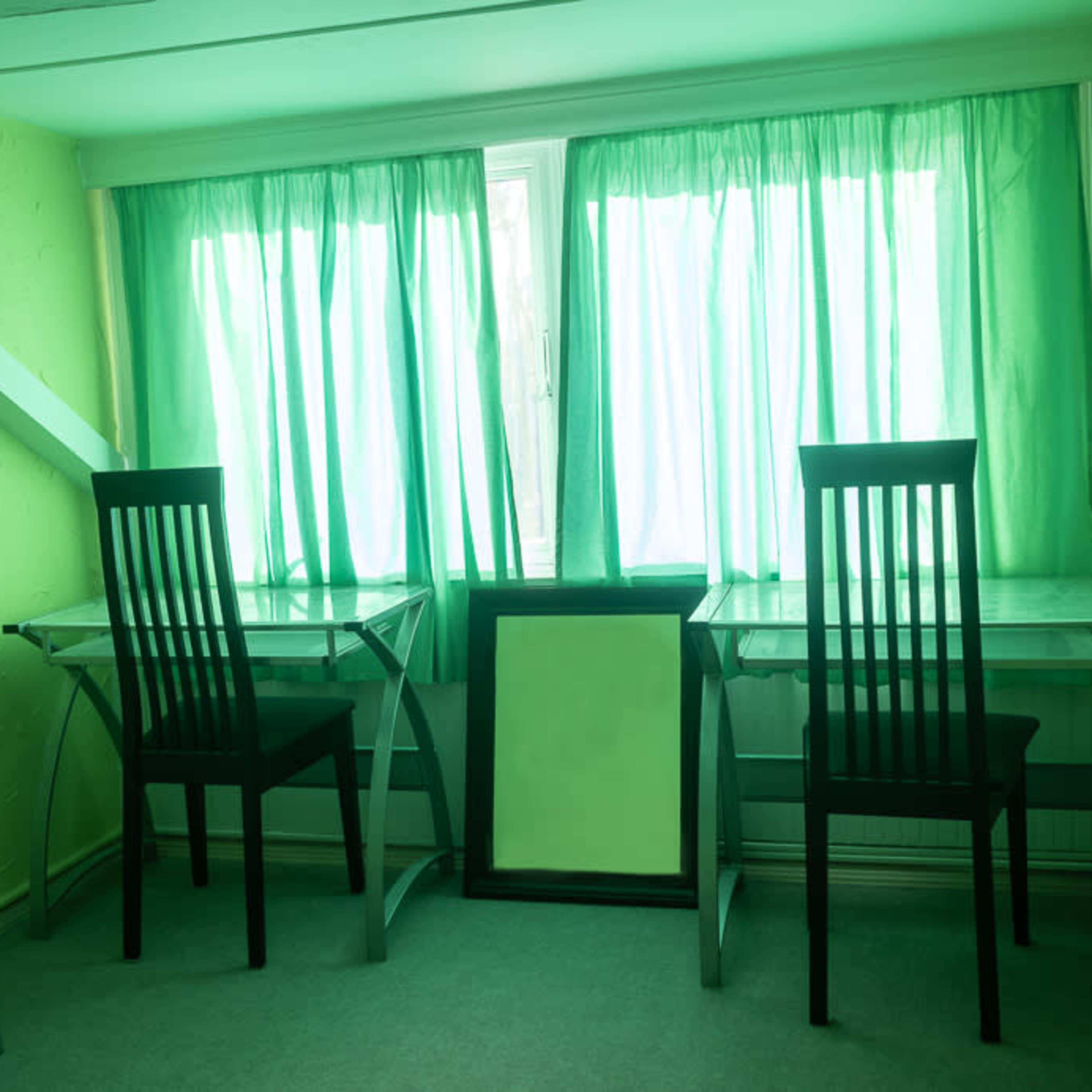 A small room with two black chairs and glass-topped tables positioned by large green curtains covering a window.