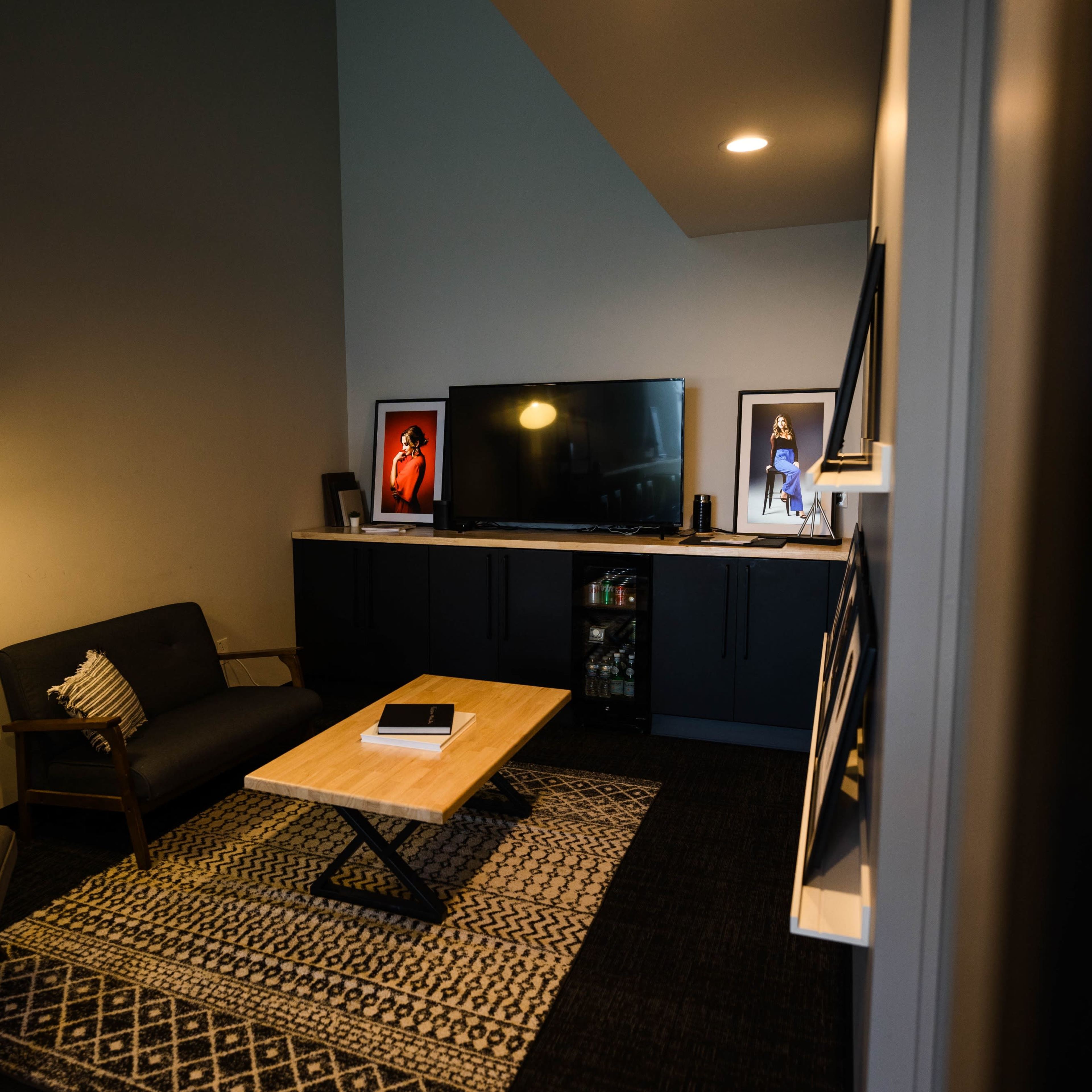A small, modern living room featuring a television, a wooden coffee table, two seating areas, and framed artwork on the walls.