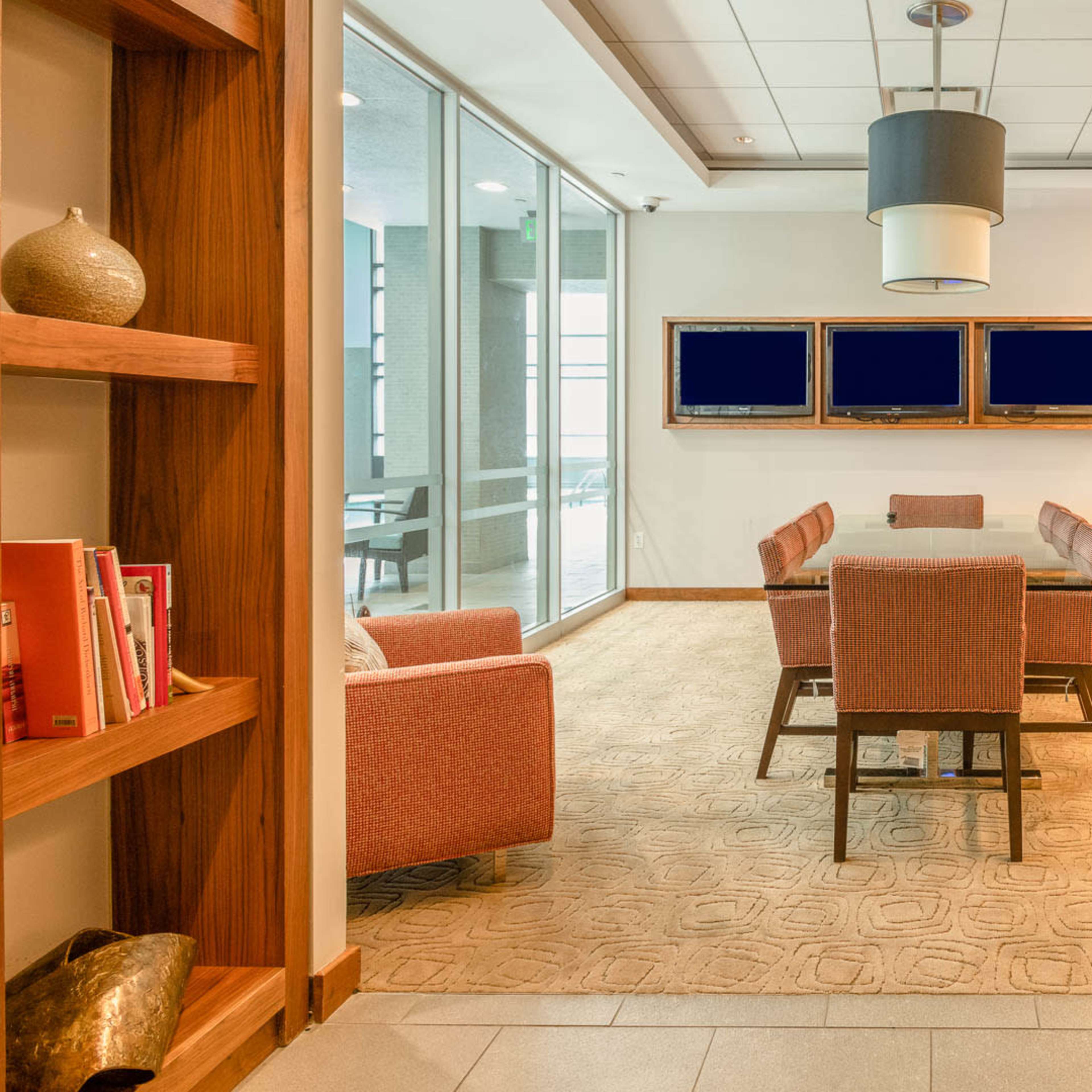 A modern meeting room with a large table, chairs, and a seating area, bordered by bookshelves filled with decorative items.